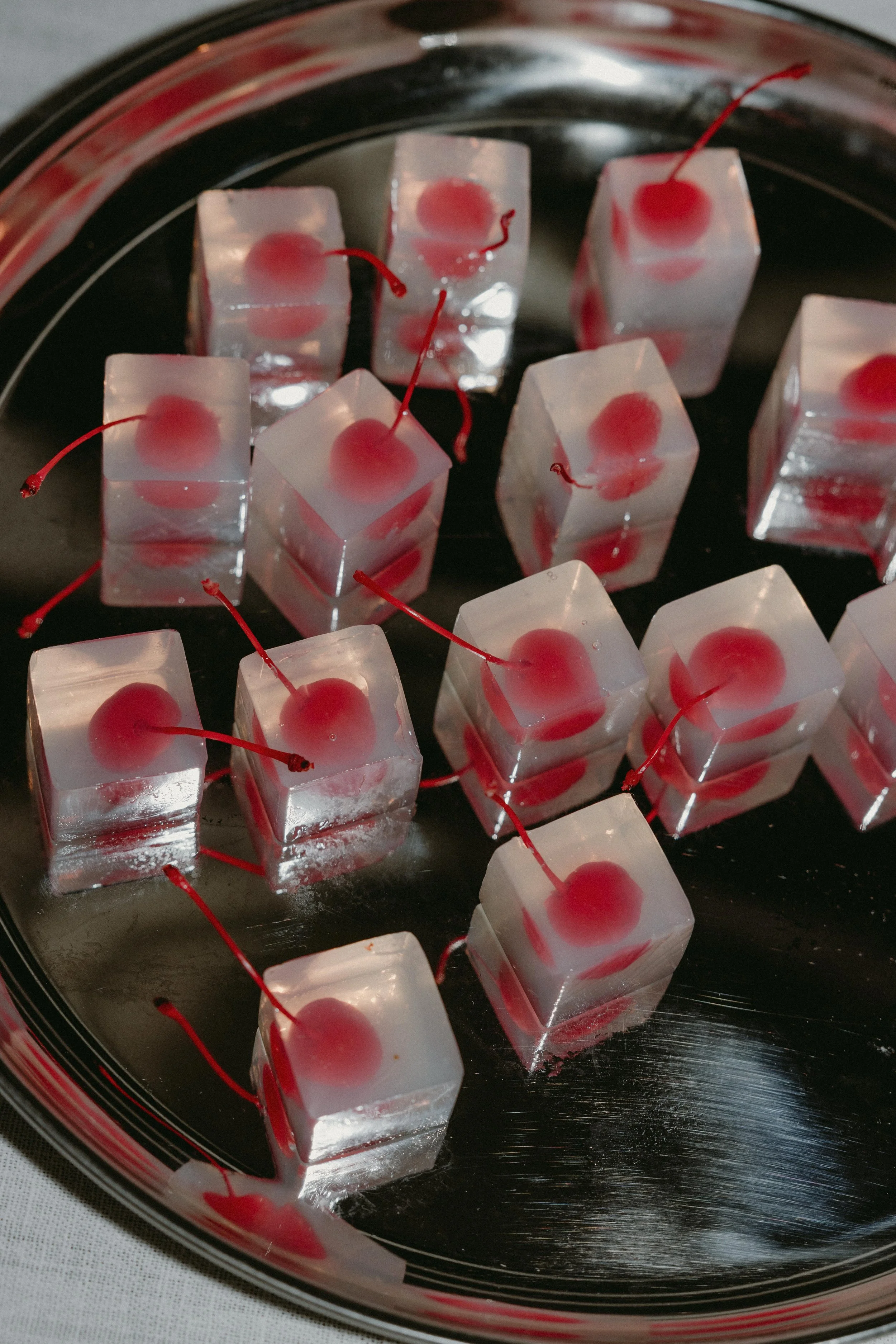 Ice cubes with cherries inside on a black tray.
