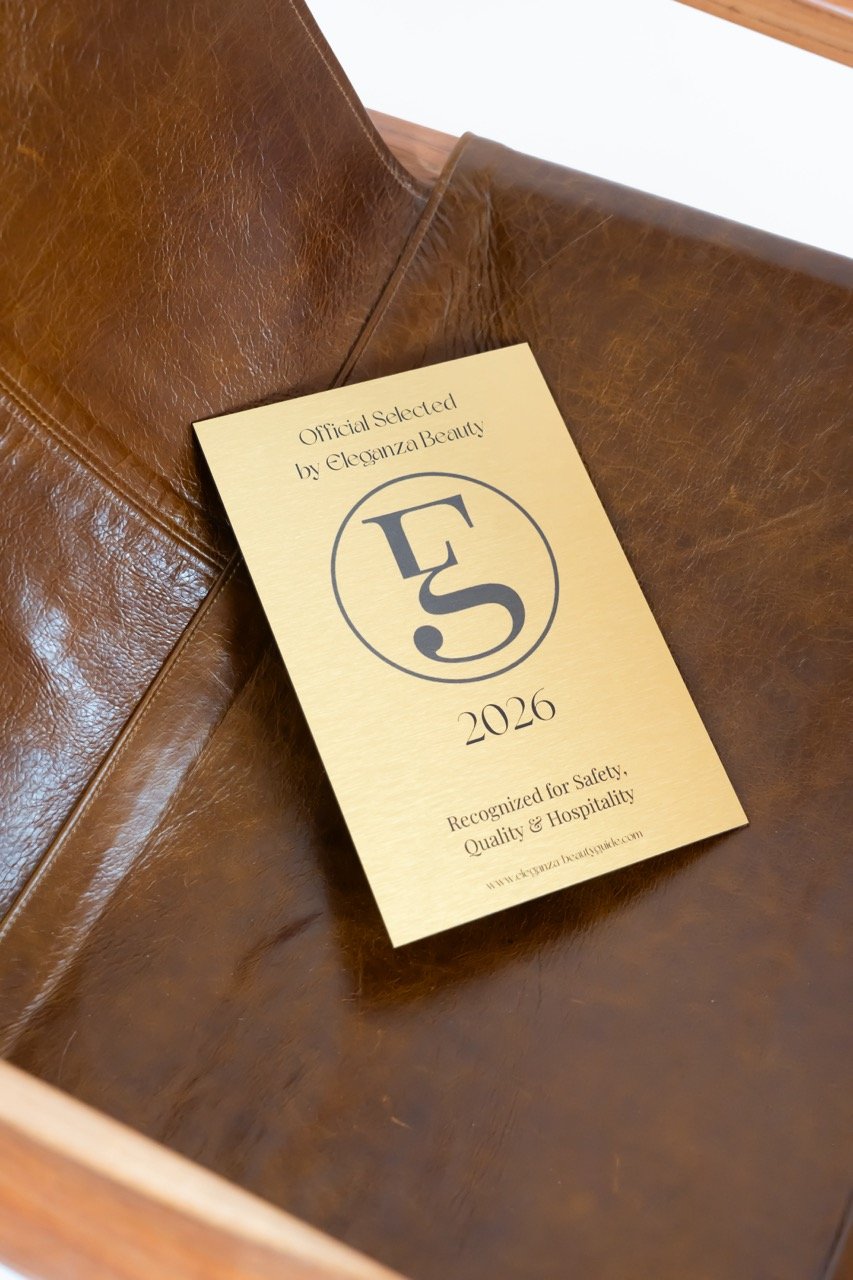A recognition award card labeled 'Official Selected by Eleganza Beauty 2026,' issued for safety, quality, and hospitality, resting inside a brown leather chair.