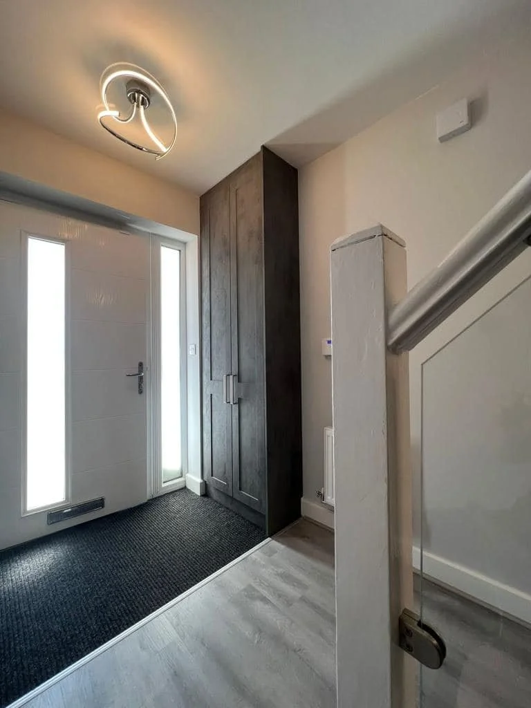 Entryway featuring a white door with glass panels, a dark wooden closet, a wall-mounted security alarm, a coat railing, and a black doormat on light-colored flooring.
