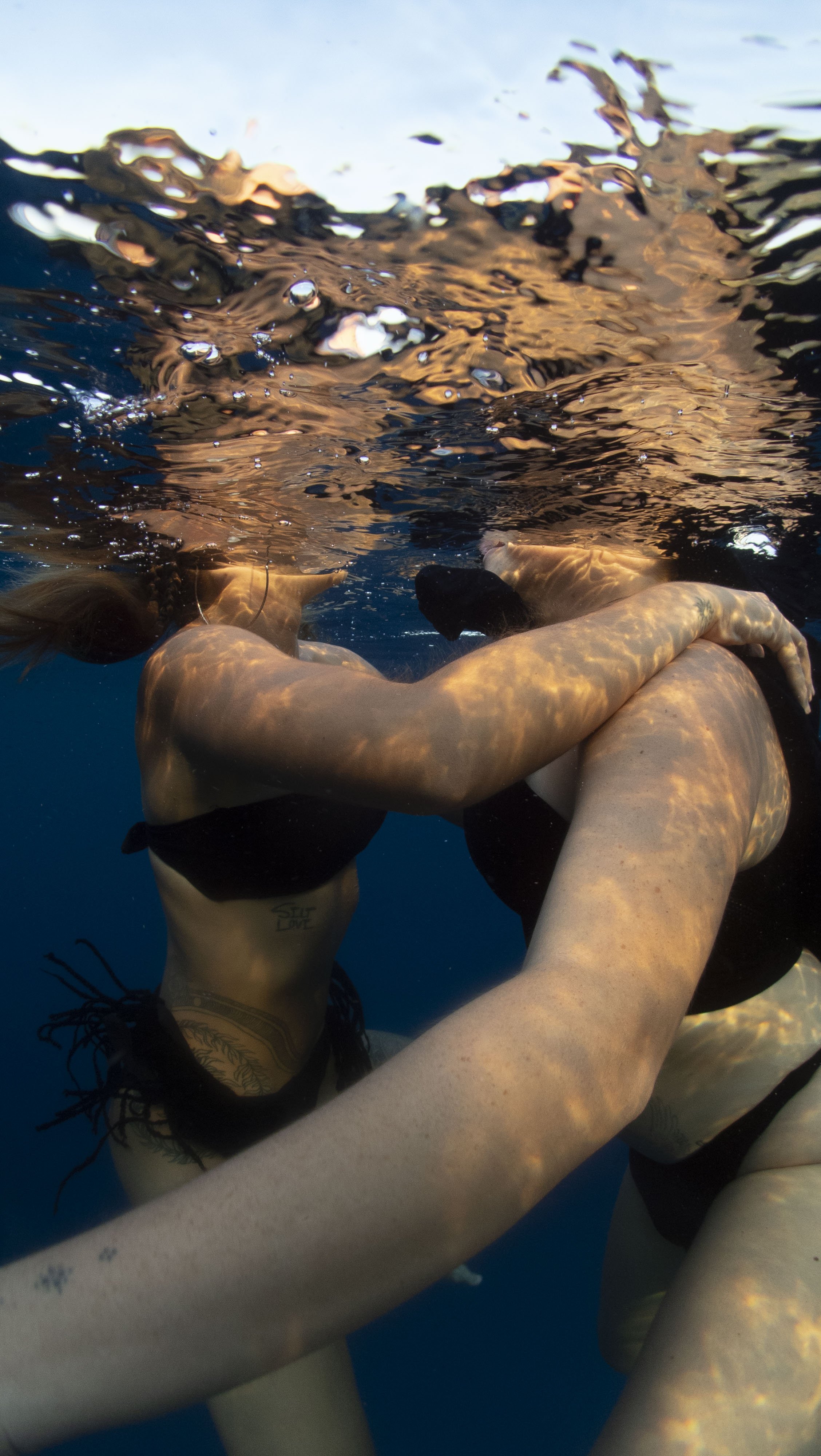Nähe zweier weiblicher Körper unterwasser. Das Licht reflektiert durchs Wasser die Wellen auf der Haut.