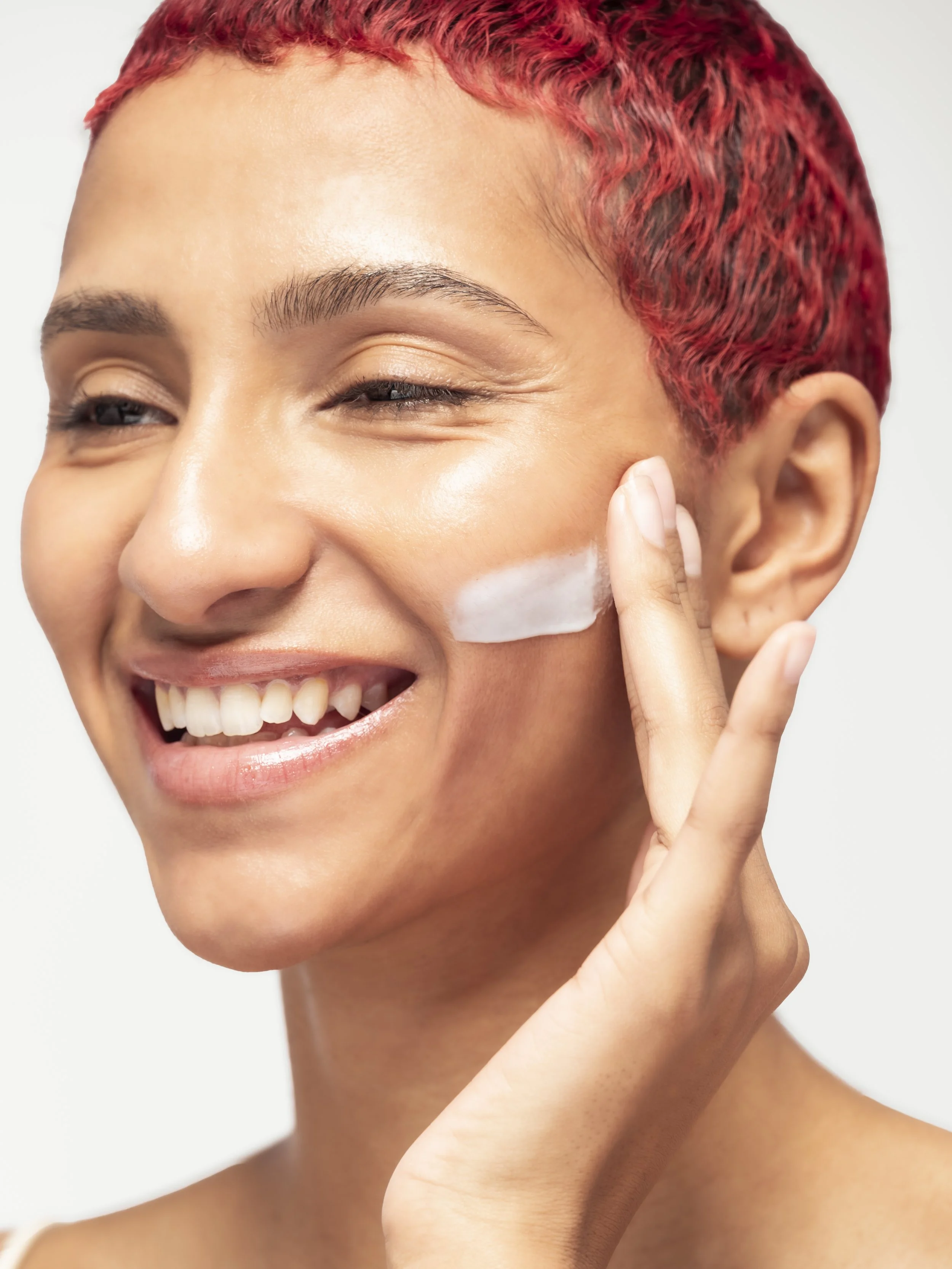 Une femme souriante appliquant de la crème sur sa joue.