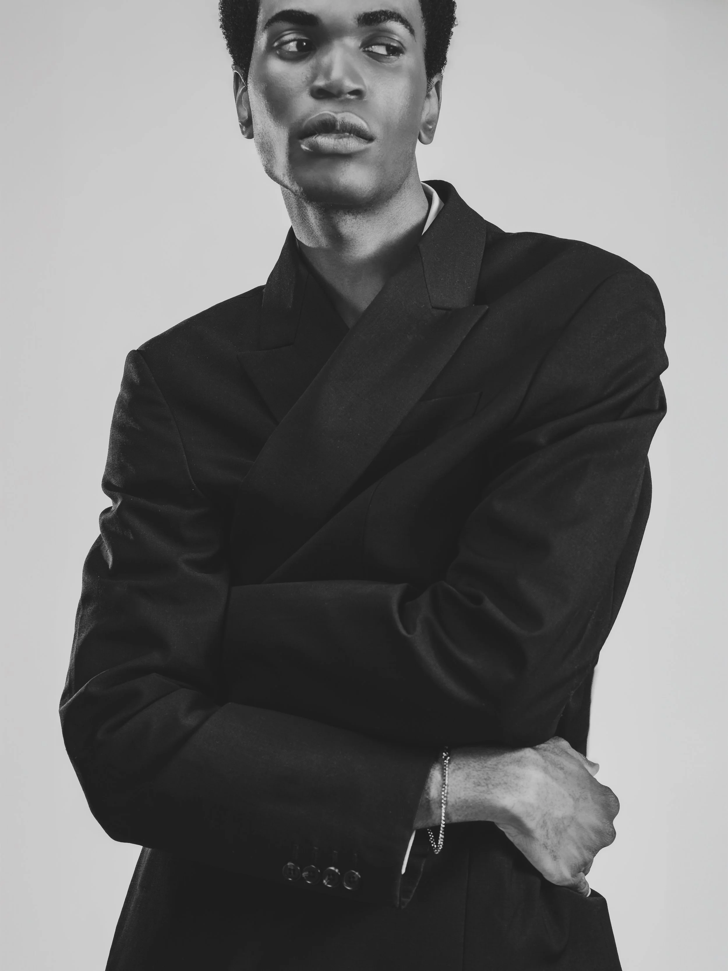 Portrait en noir et blanc d'une personne portant une veste sombre, regardant vers la gauche avec les bras croisés.