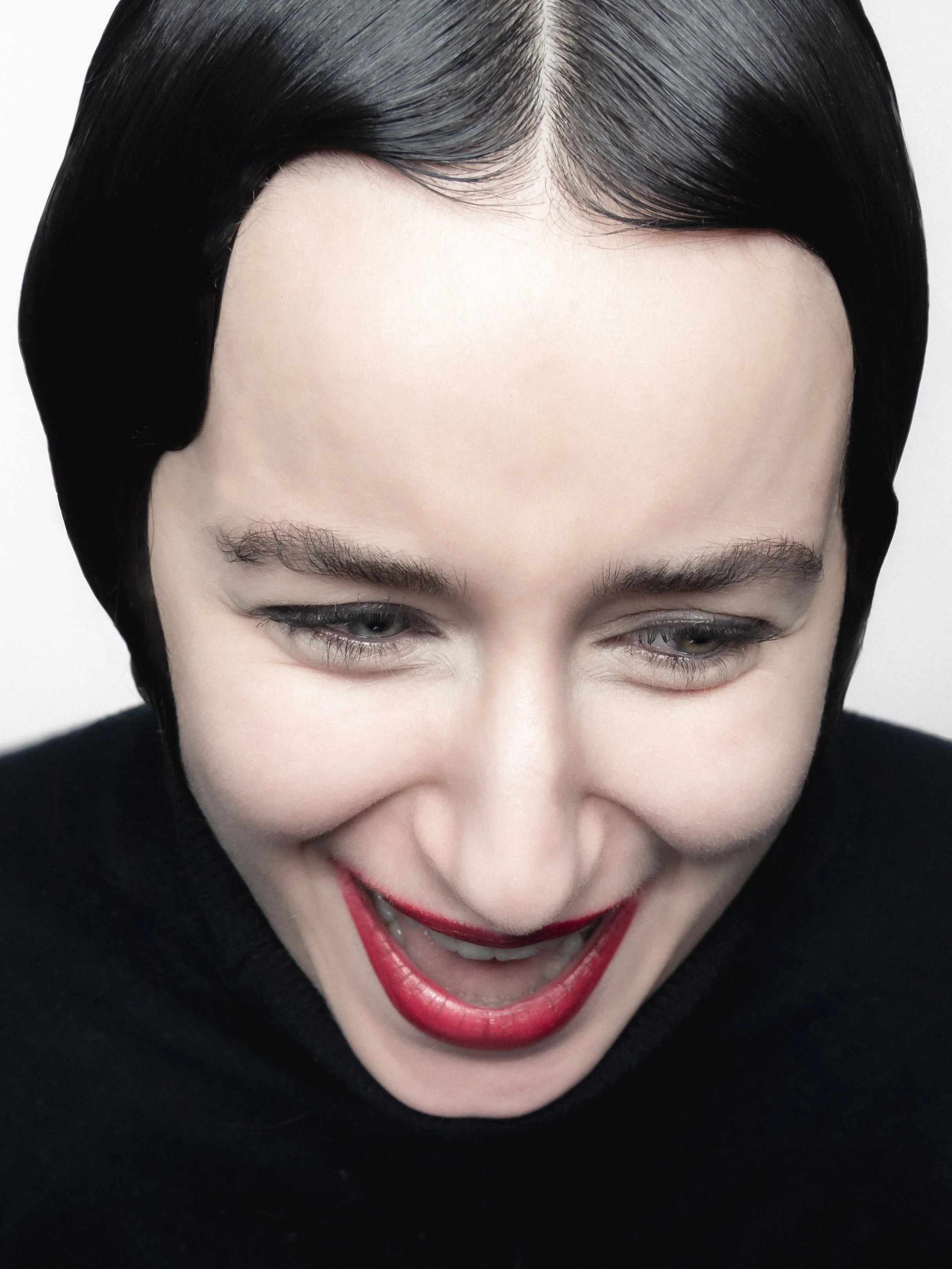 Photo d'une femme avec une coiffure noire, souriant avec les yeux presque fermés, portant du maquillage rouge à lèvres, portrait en gros plan.