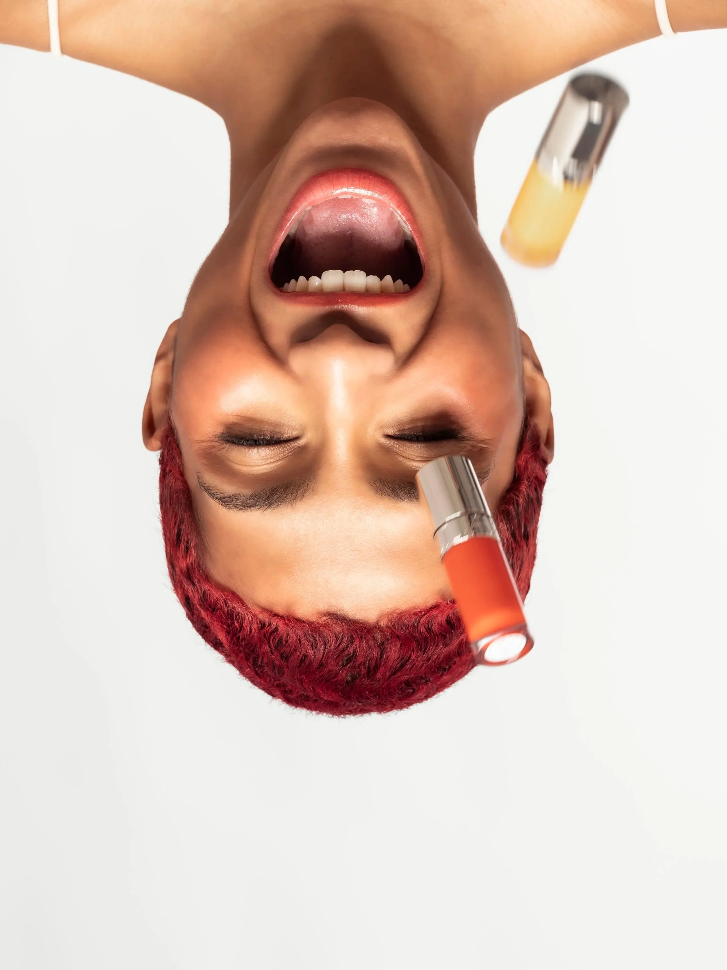 Personne avec des cheveux rouges, yeux fermés, bouche ouverte, deux bouteilles de parfum flottant autour d'elle, fond blanc.