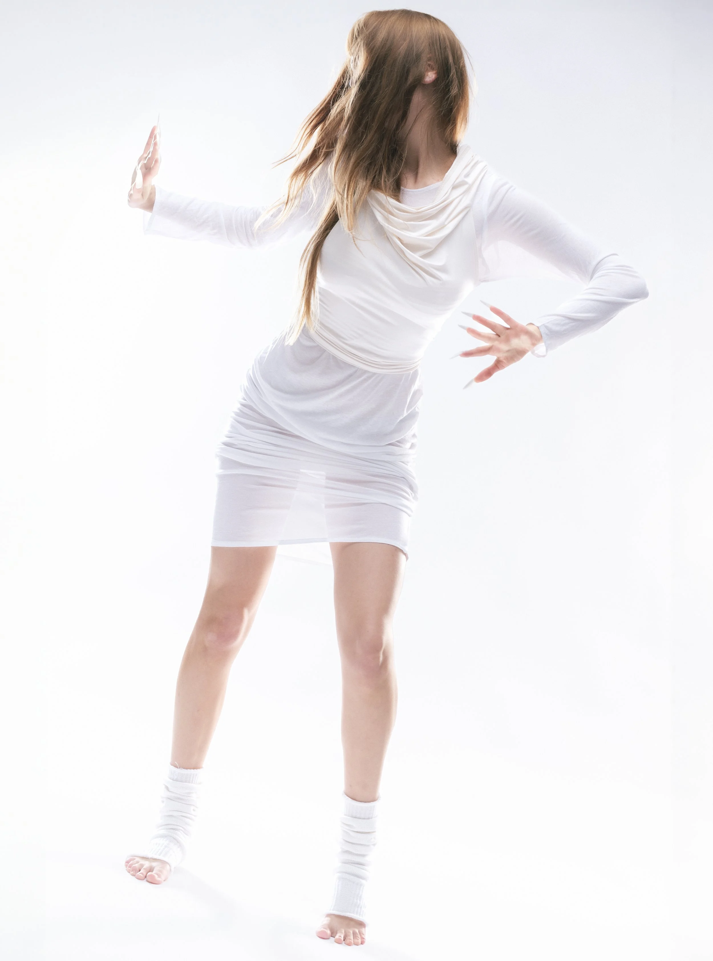 Femme portant une robe blanche en mouvement, les bras levés et la tête tournée, sur fond blanc.