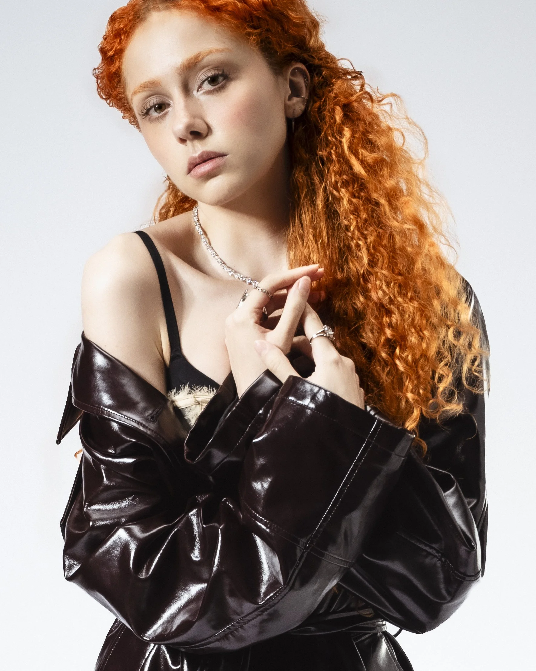 Jeune femme aux cheveux roux, portant un manteau en cuir, bijoux en argent, posé contre un fond blanc.
