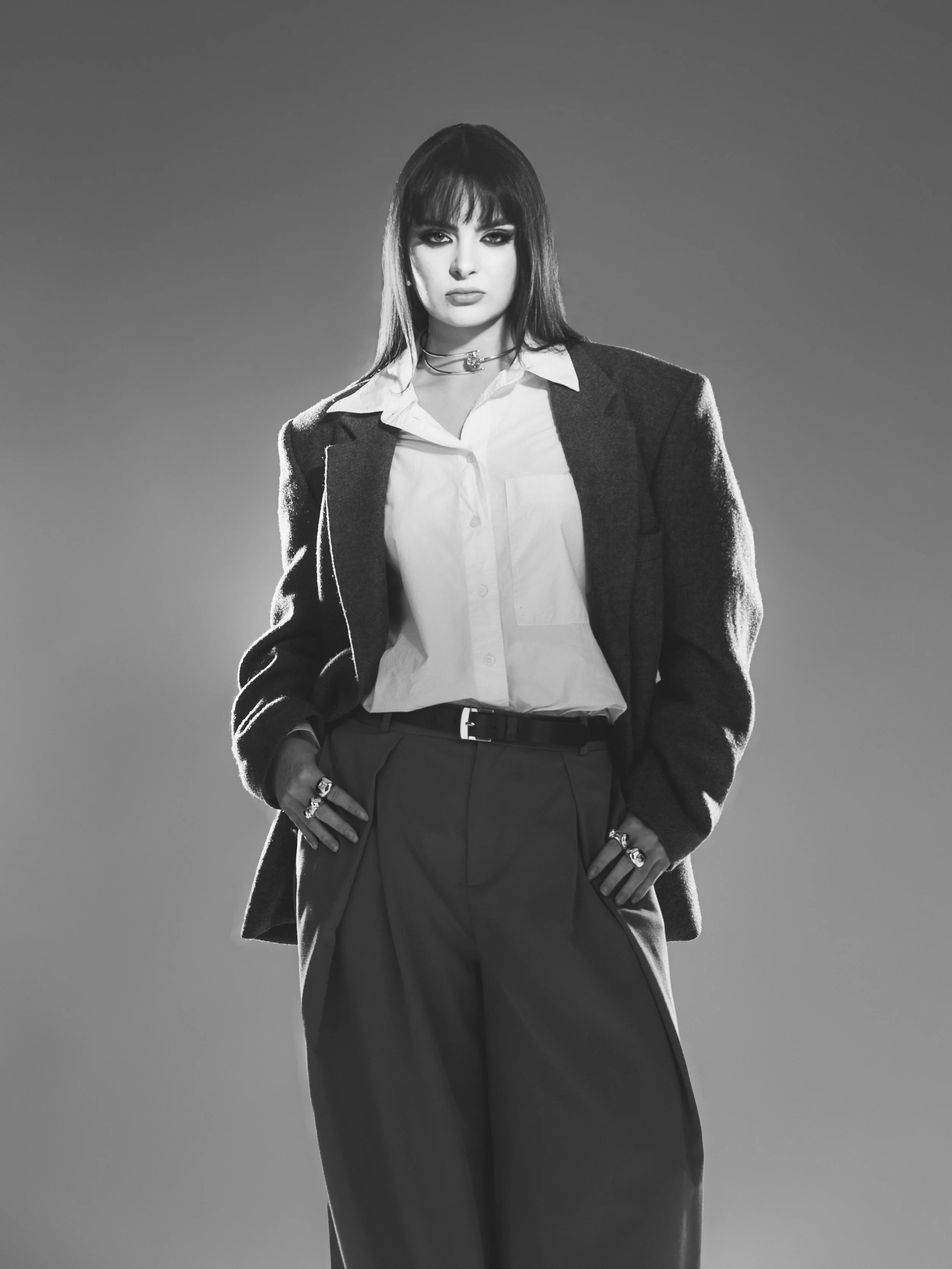 Une femme habillée en tailleur noir avec une chemise blanche, posant avec confiance. Photographie en noir et blanc.