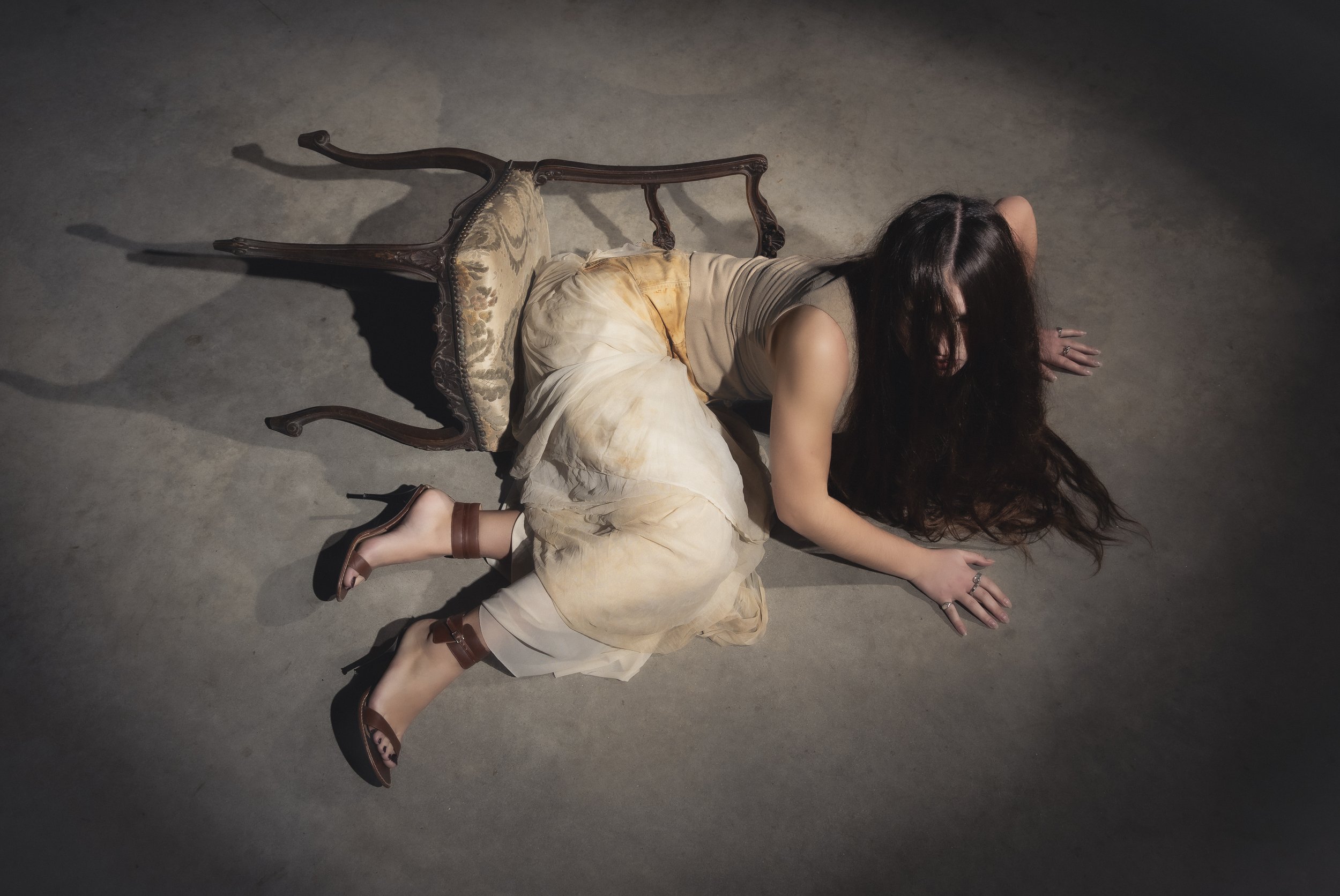 Une femme allongée sur le sol, appuyée sur ses mains et ses genoux, avec un fauteuil inversé derrière elle.