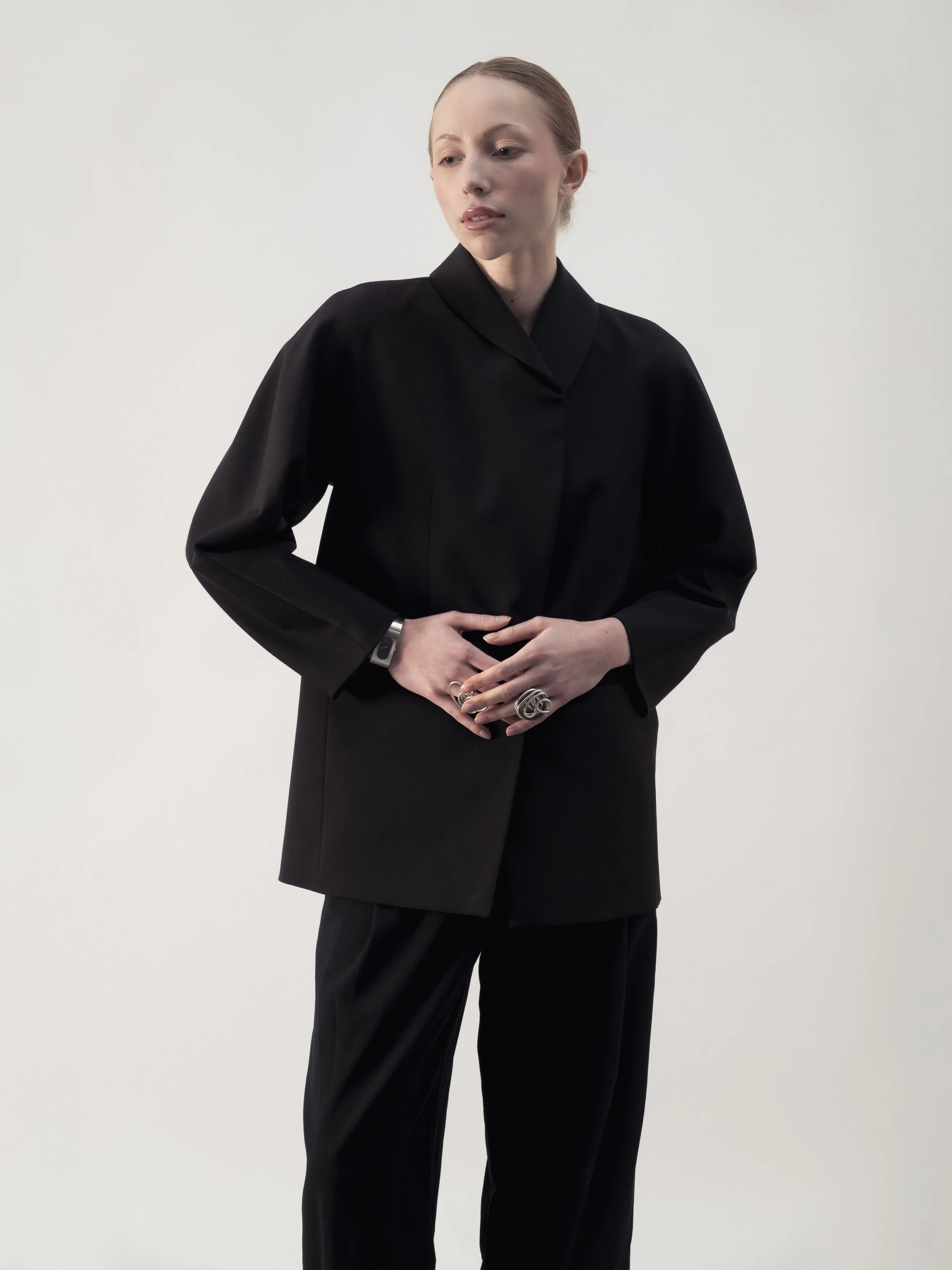 Une femme portant un costume noir avec des bijoux argentés, posant devant un fond blanc.