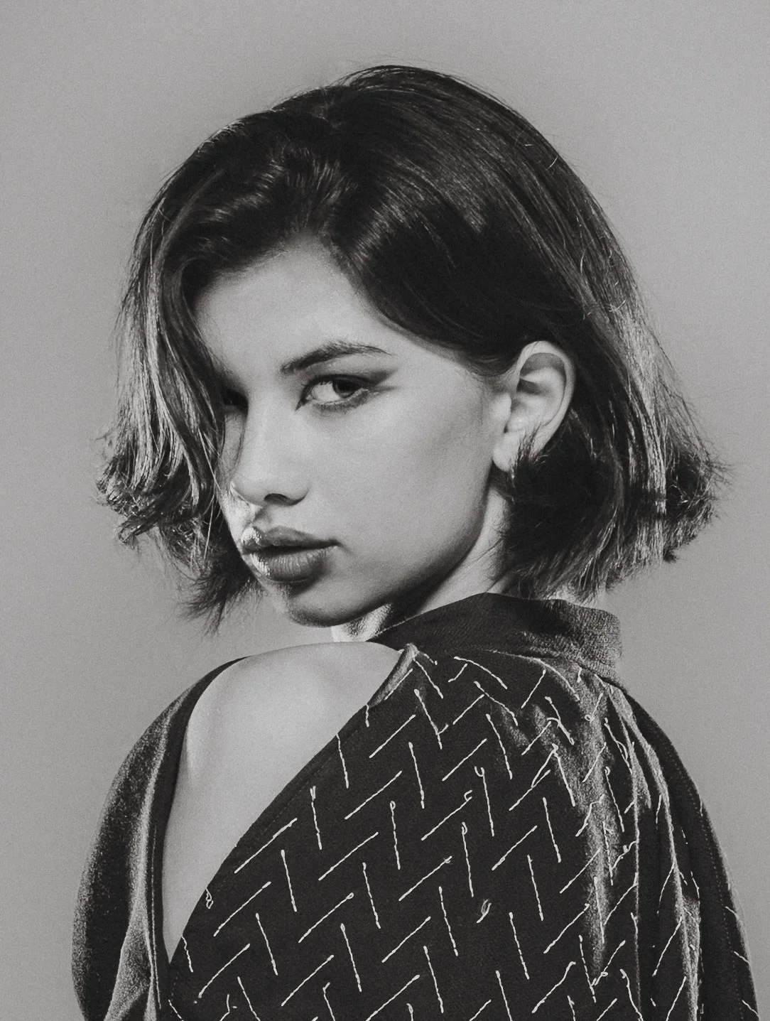 Portrait en noir et blanc d'une femme avec des cheveux courts et ondulés, portant un vêtement avec un motif à rayures diagonales.