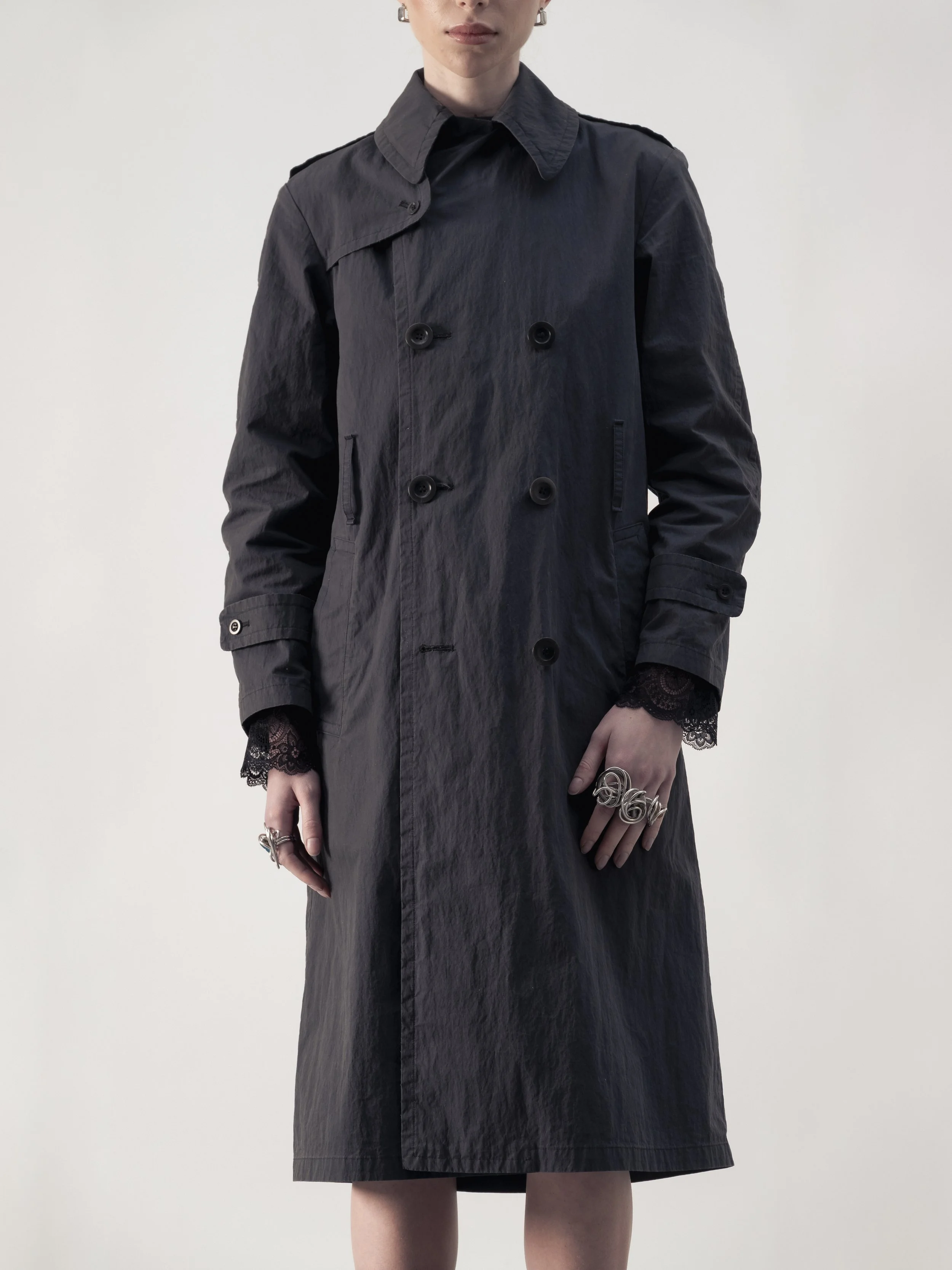 Femme portant un trench noir avec des bijoux et des manches en dentelle.