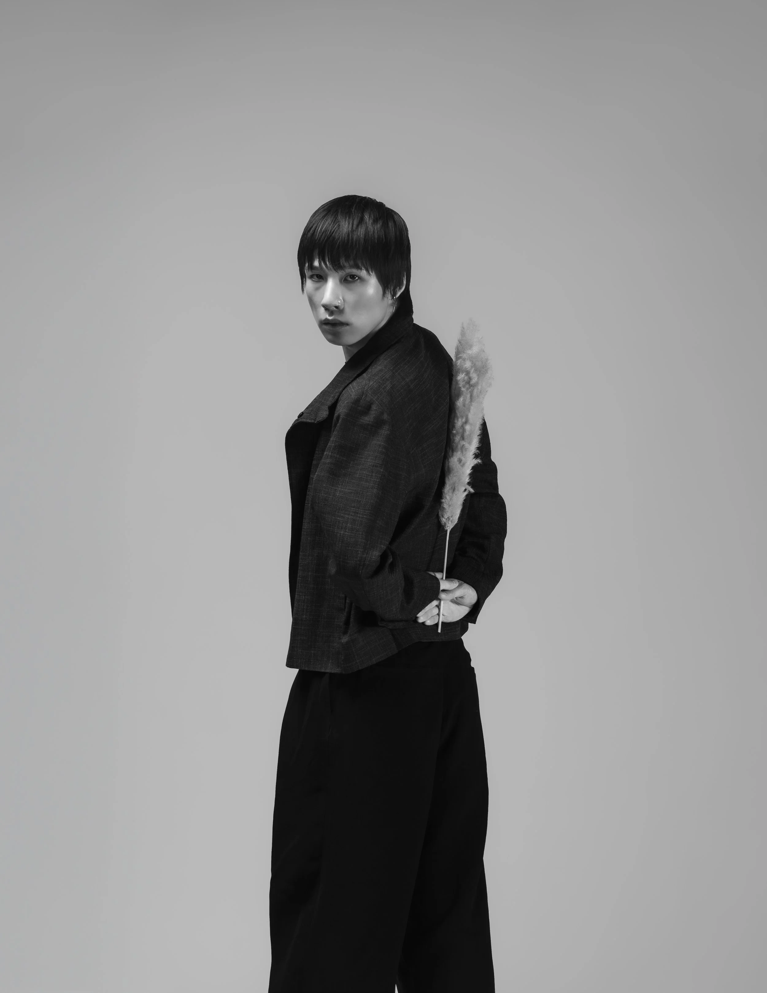 Un homme en vêtement noir, tenant une plume de coton, regarde vers l'objectif, photo en noir et blanc.