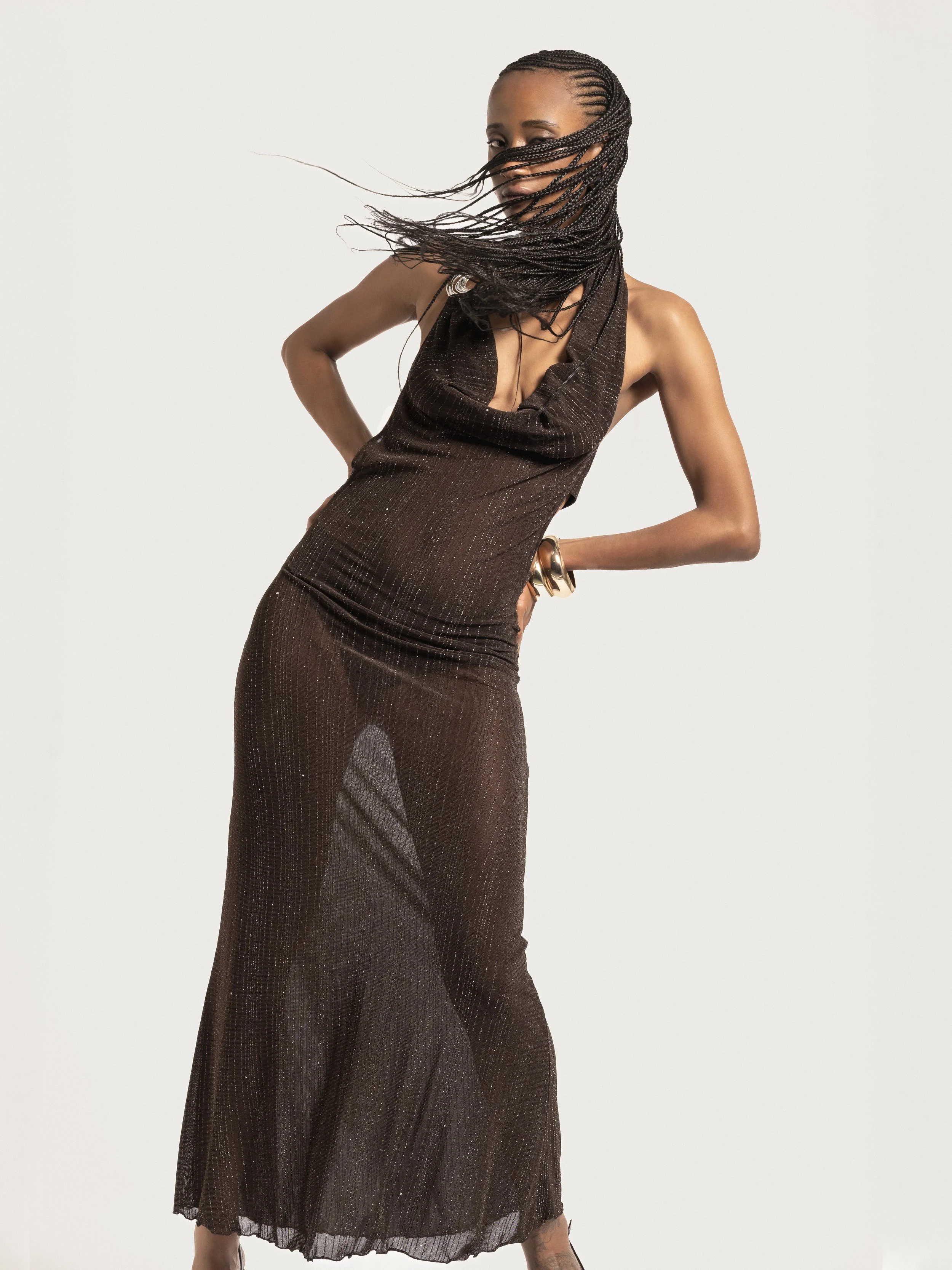 Femme portant une robe longue brune en mouvement, cheveux tressés, pose dynamique.