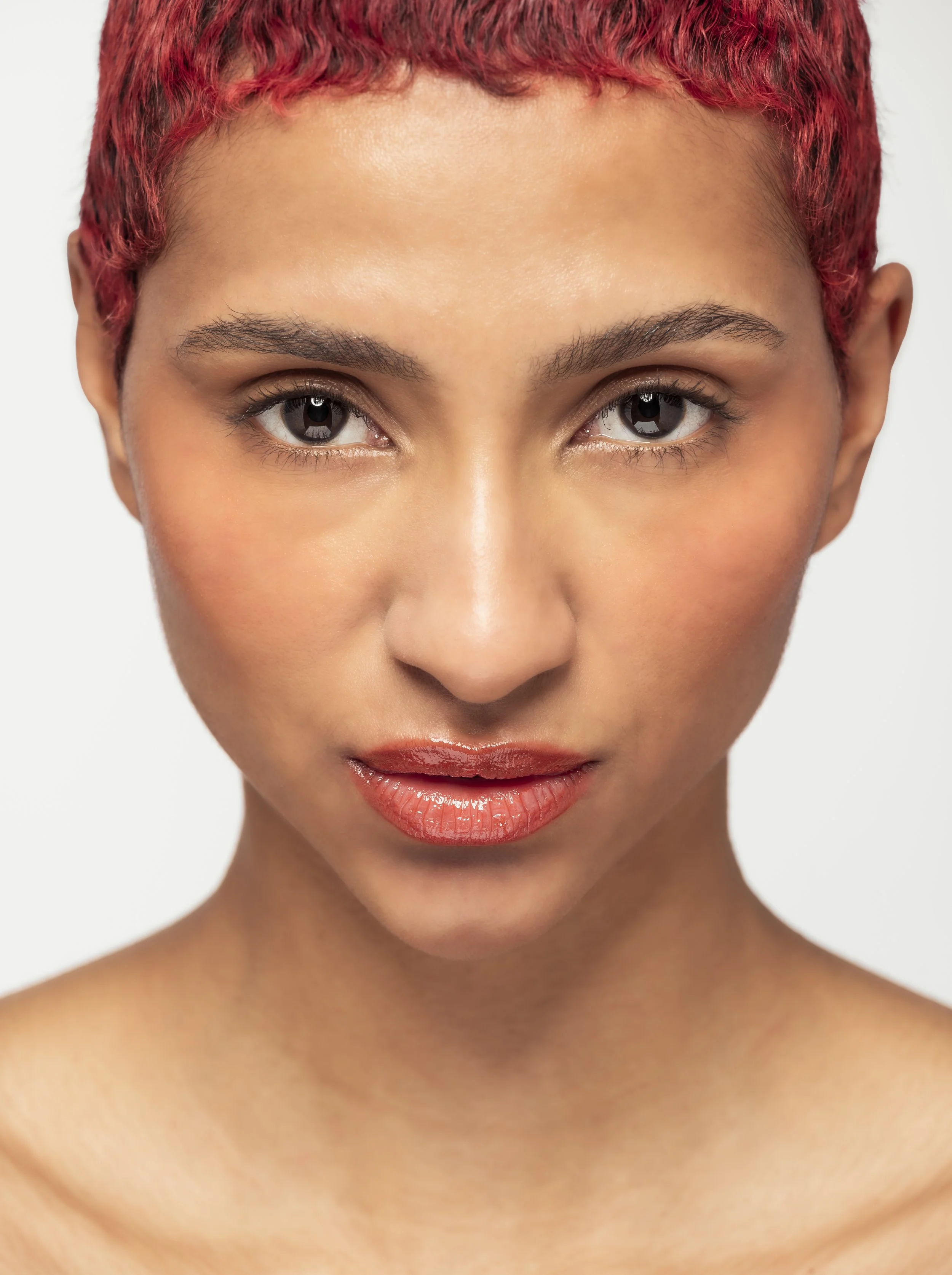 Portrait d'une femme avec des cheveux courts, recourbés, colorés en rouge, portant un maquillage naturel et un lipstick lumineux