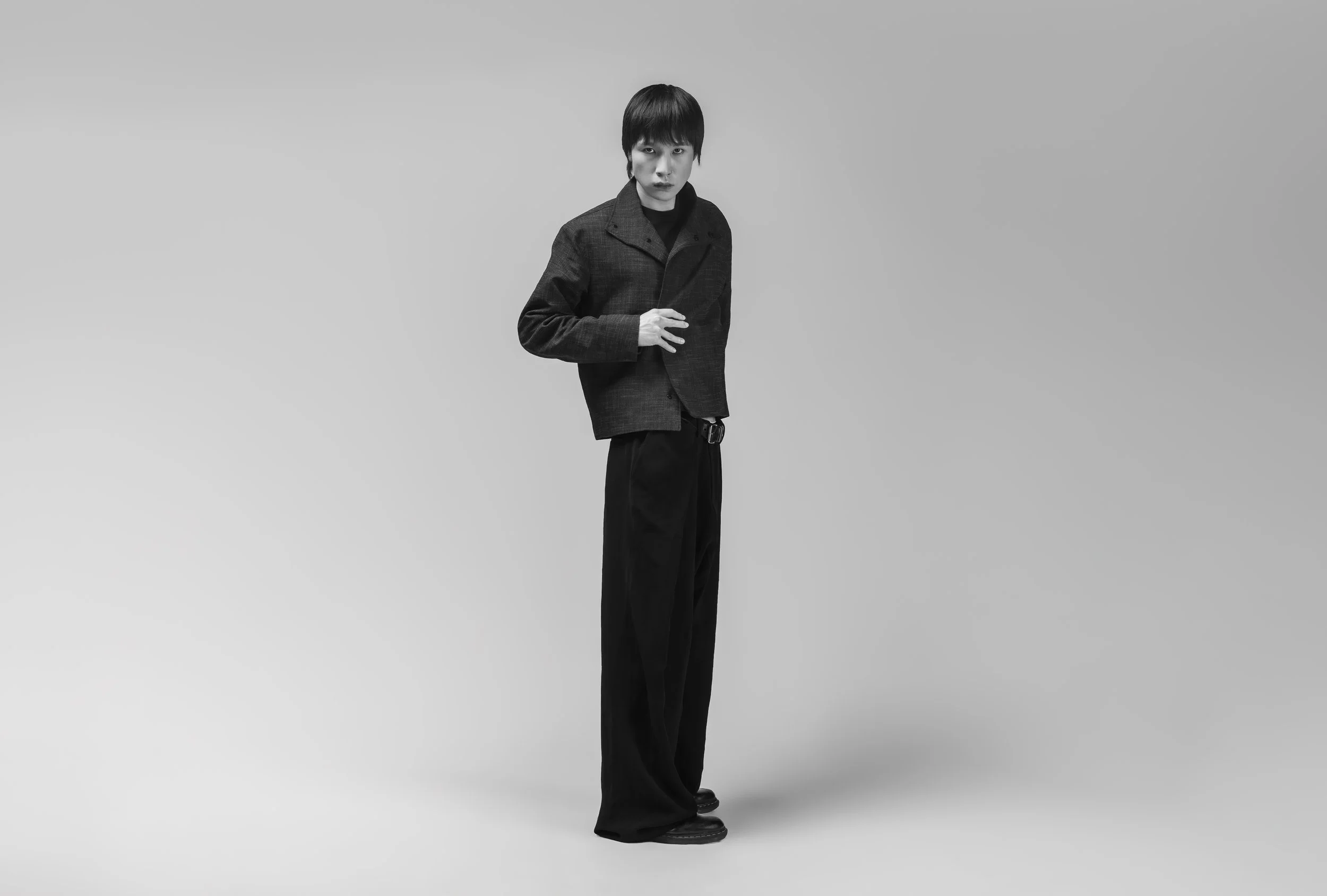 Une femme en vêtements noirs, cheveux courts, pose dans un studio vide en noir et blanc.