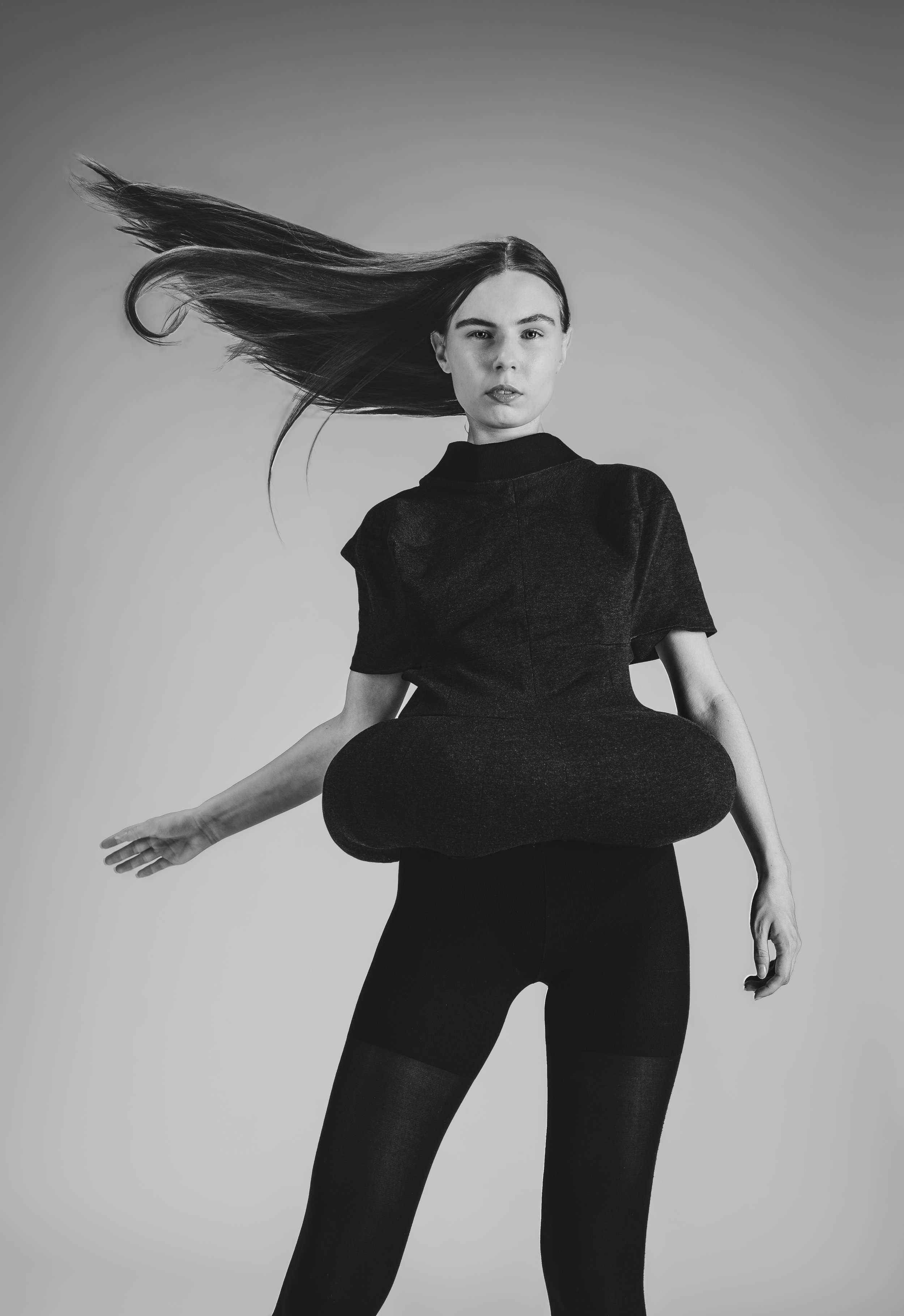 Une femme en noir et blanc portant une tenue noire, avec ses cheveux longs et droits qui flottent dans l'air.