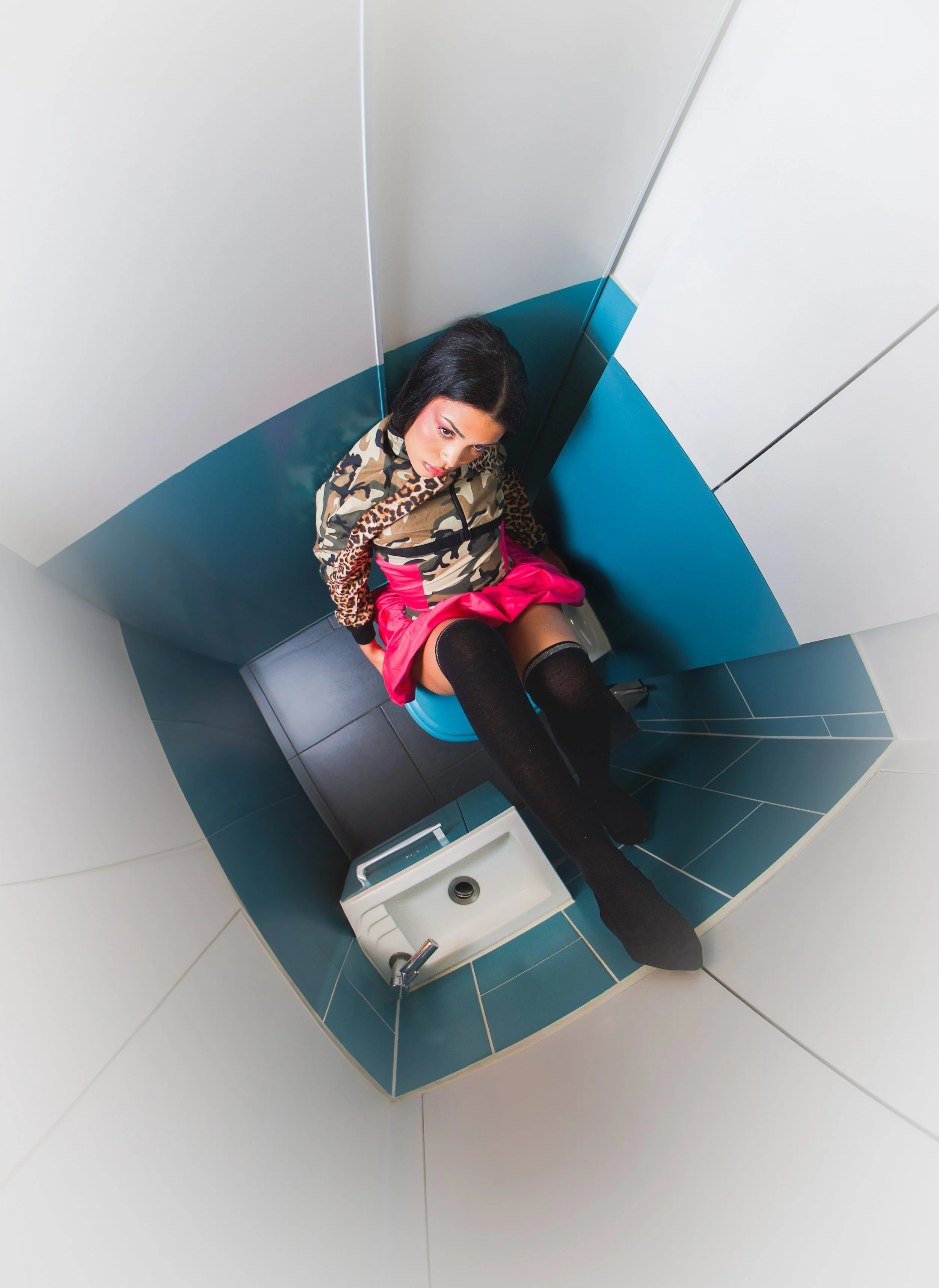 Jeune femme dans des vêtements colorés assise sur des toilettes, vue du dessus, dans une cabine de toilettes modernes.