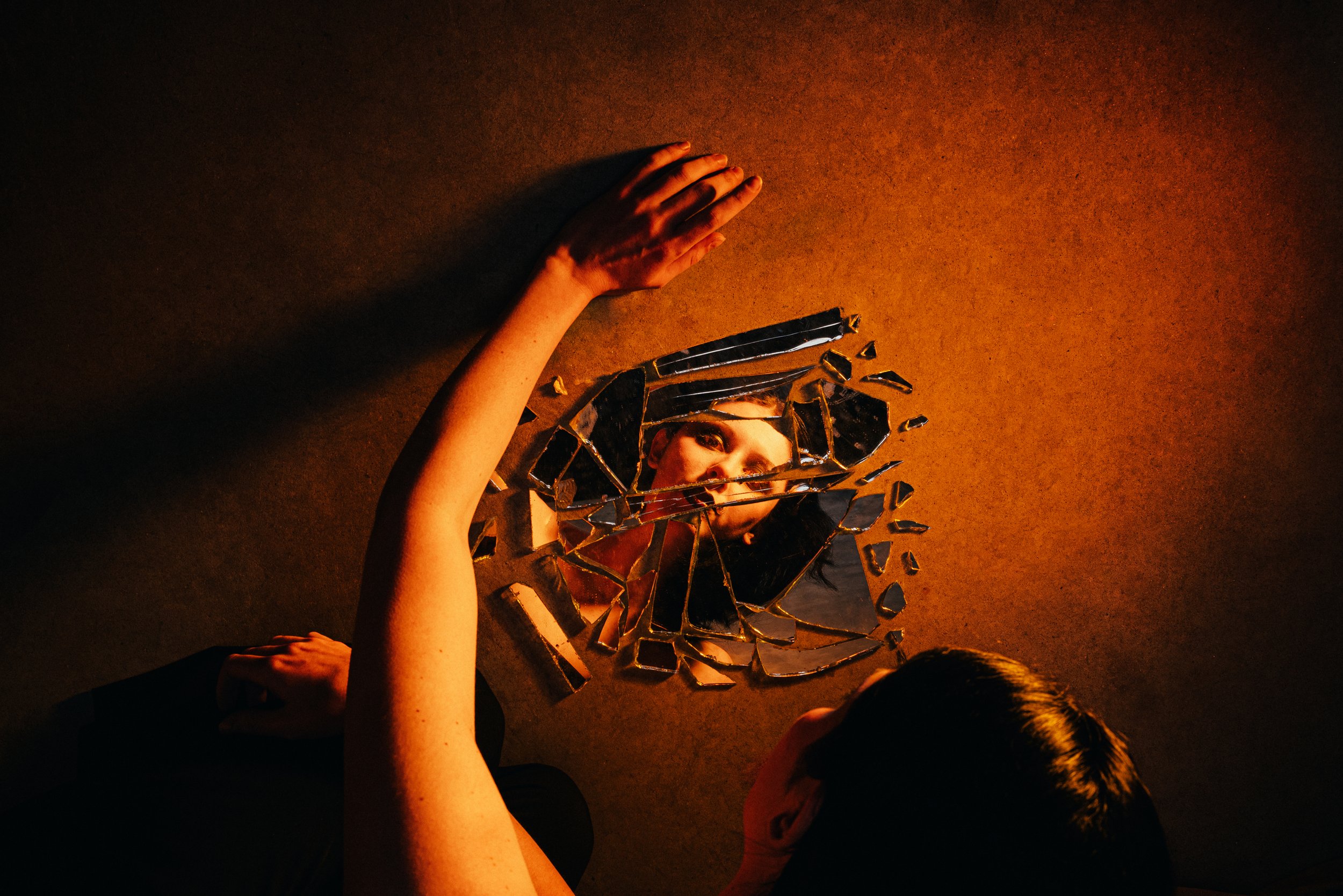 Une personne regarde dans un miroir brisé, la photo est prise du dessus, avec un éclairage chaud.