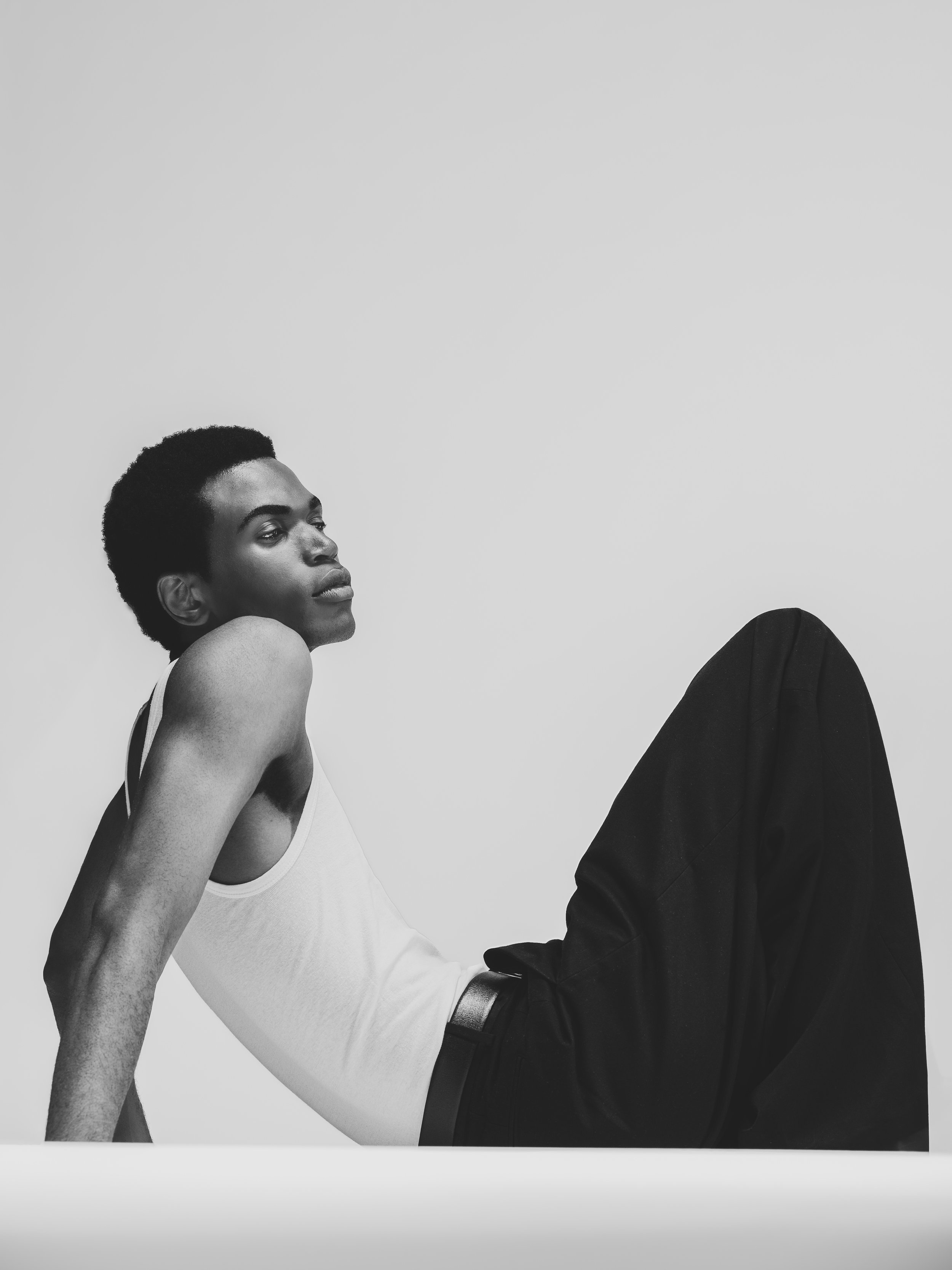 Jeune femme noire en vêtements décontractés, assise contre un mur blanc.