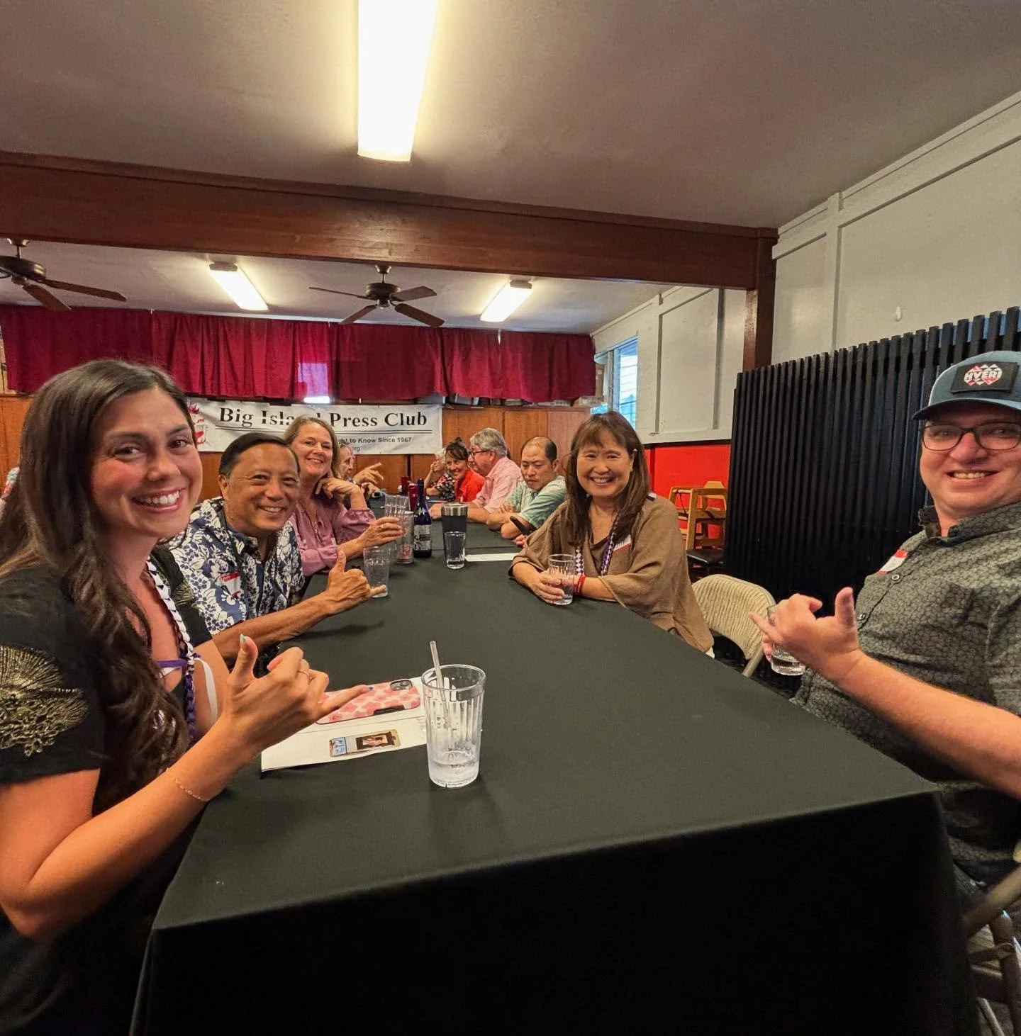Group of people sitting at a long table during a gathering at the Big Island Press Club, smiling and looking at the camera.