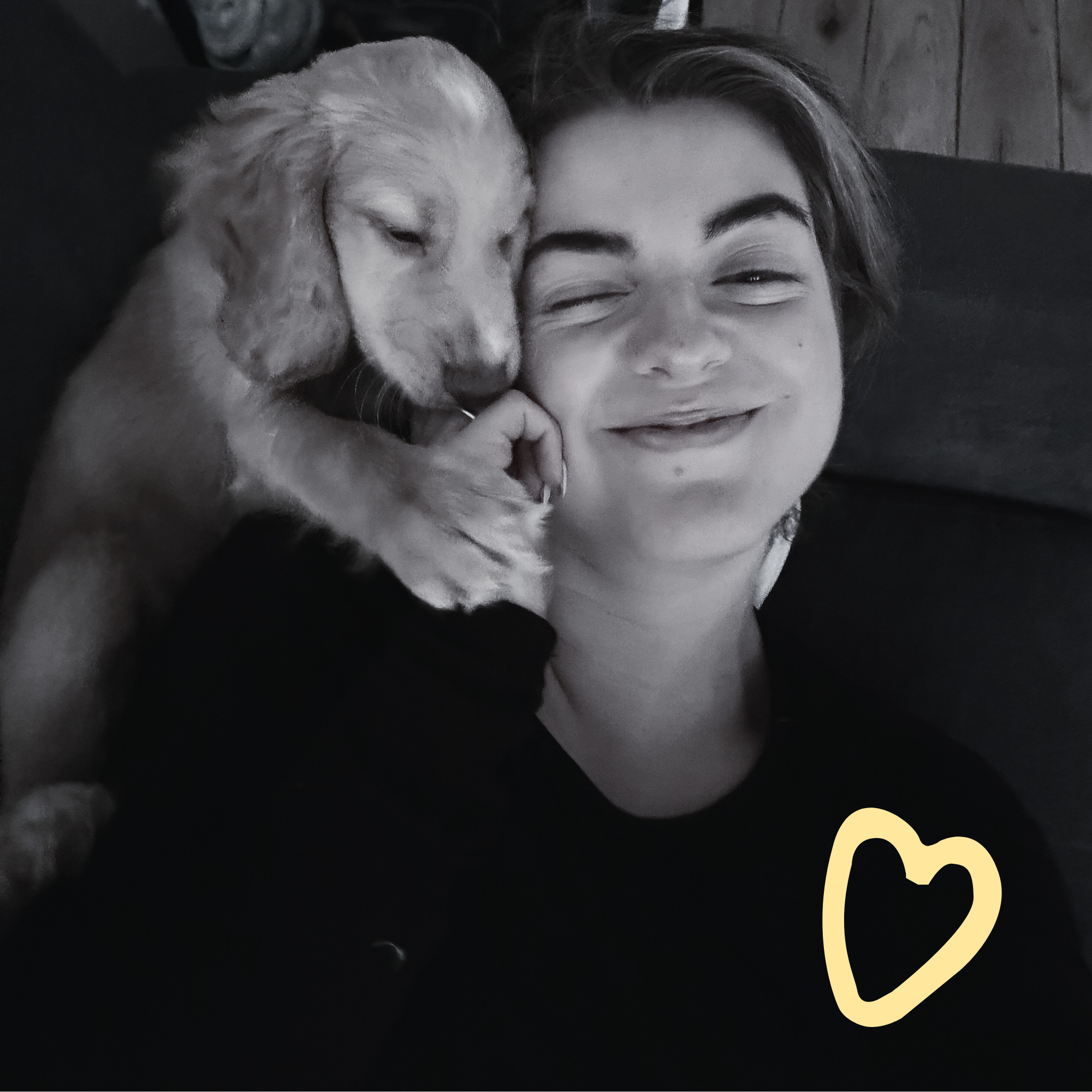 Een persoon met kort haar ligt op een bankje of bed met een knuffel of puppy die dicht tegen haar/hem aan ligt, beiden glimlachen. Gevraagd om de inhoud van de afbeelding in het Nederlands.