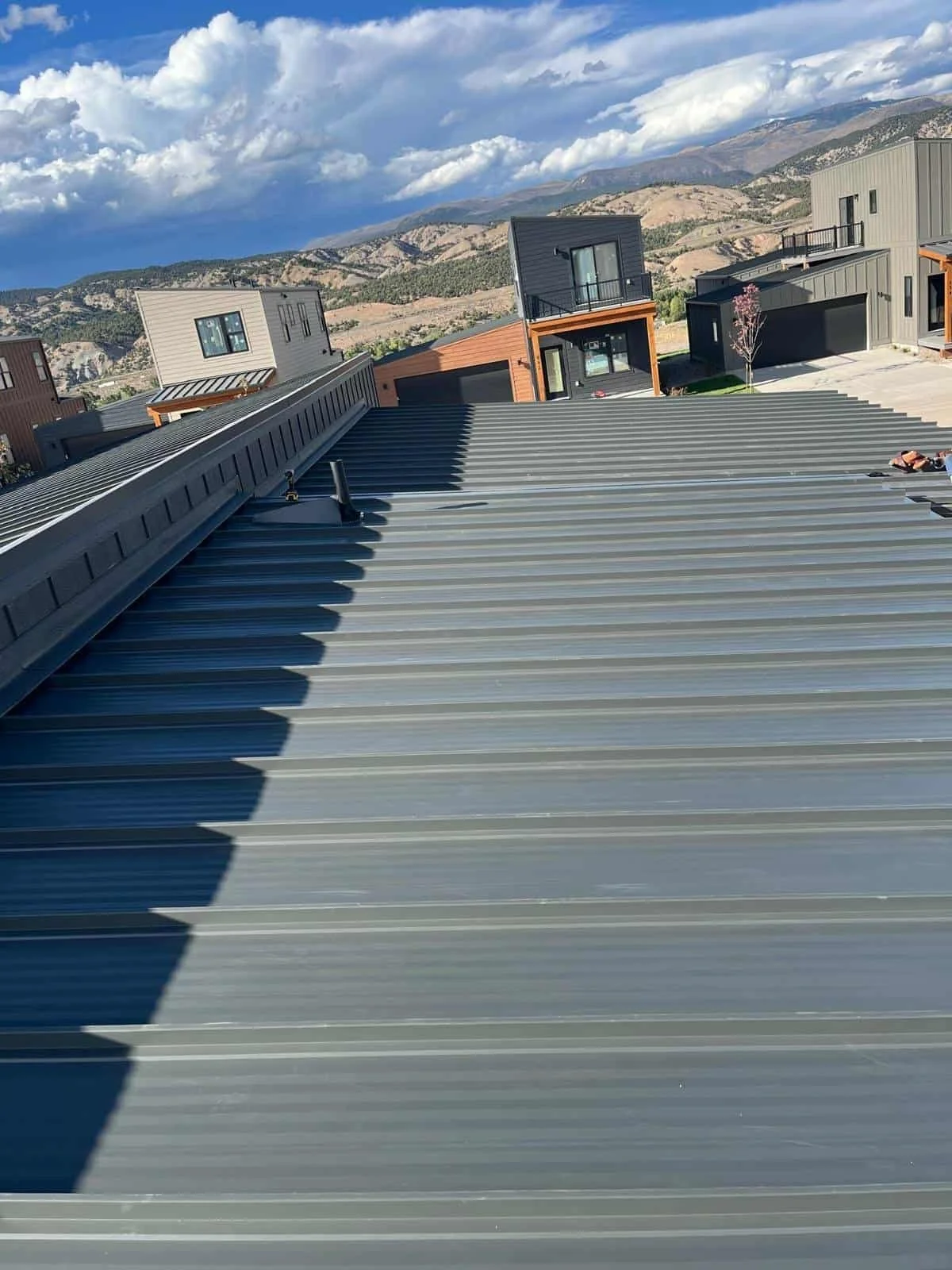 View from the roof of a modern residential building showing neighboring houses with mountains in the background and a partly cloudy sky.