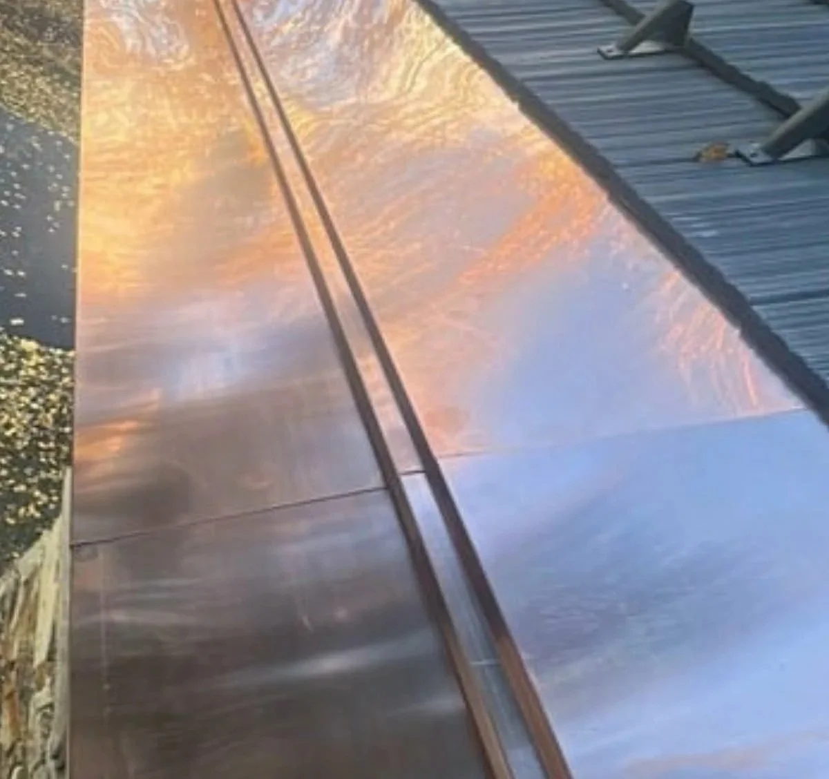 Close-up of a shiny metallic surface reflecting a sunset with trees, a roof with shingles, and a cloudy sky.
