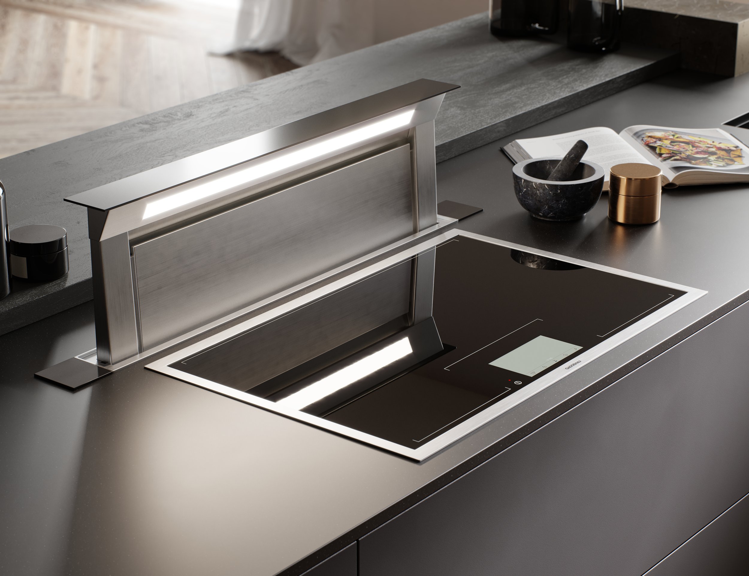Modern kitchen with an induction cooktop and a built-in range hood on a gray countertop, with an open cookbook, a mortar and pestle, a gold container, and a few small objects nearby.