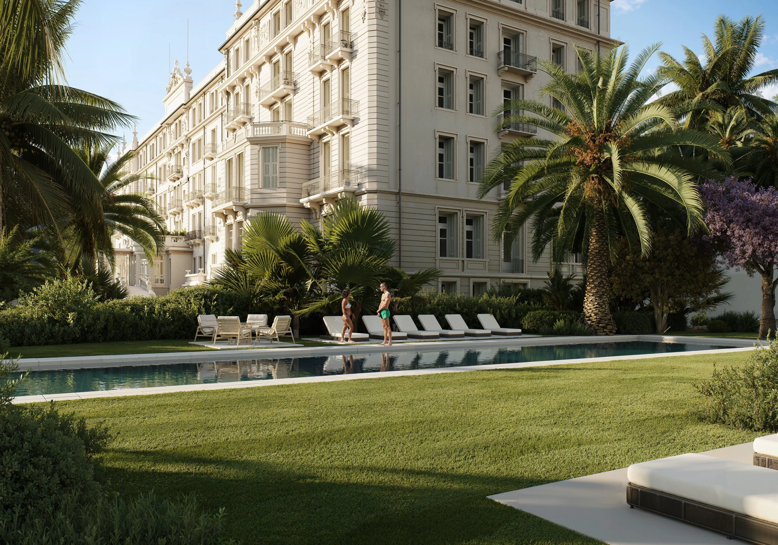 People standing by a pool in front of a large, white, multi-story hotel or apartment building surrounded by tropical trees and poolside lounge chairs.