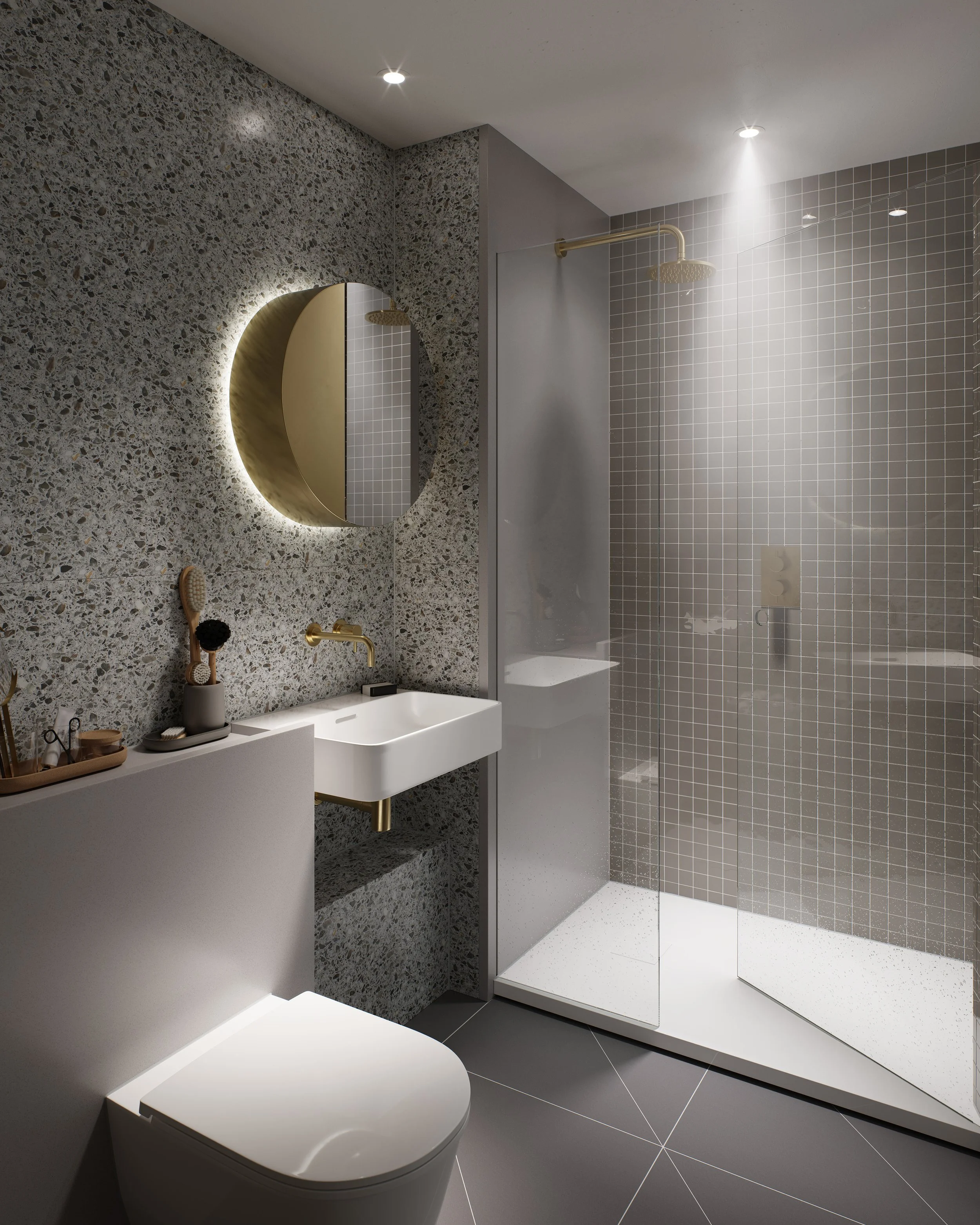 Modern bathroom with a terrazzo wall, illuminated round mirror, white sink with gold accents, and a glass-enclosed shower area with gray tiled walls and ceiling-mounted shower head.