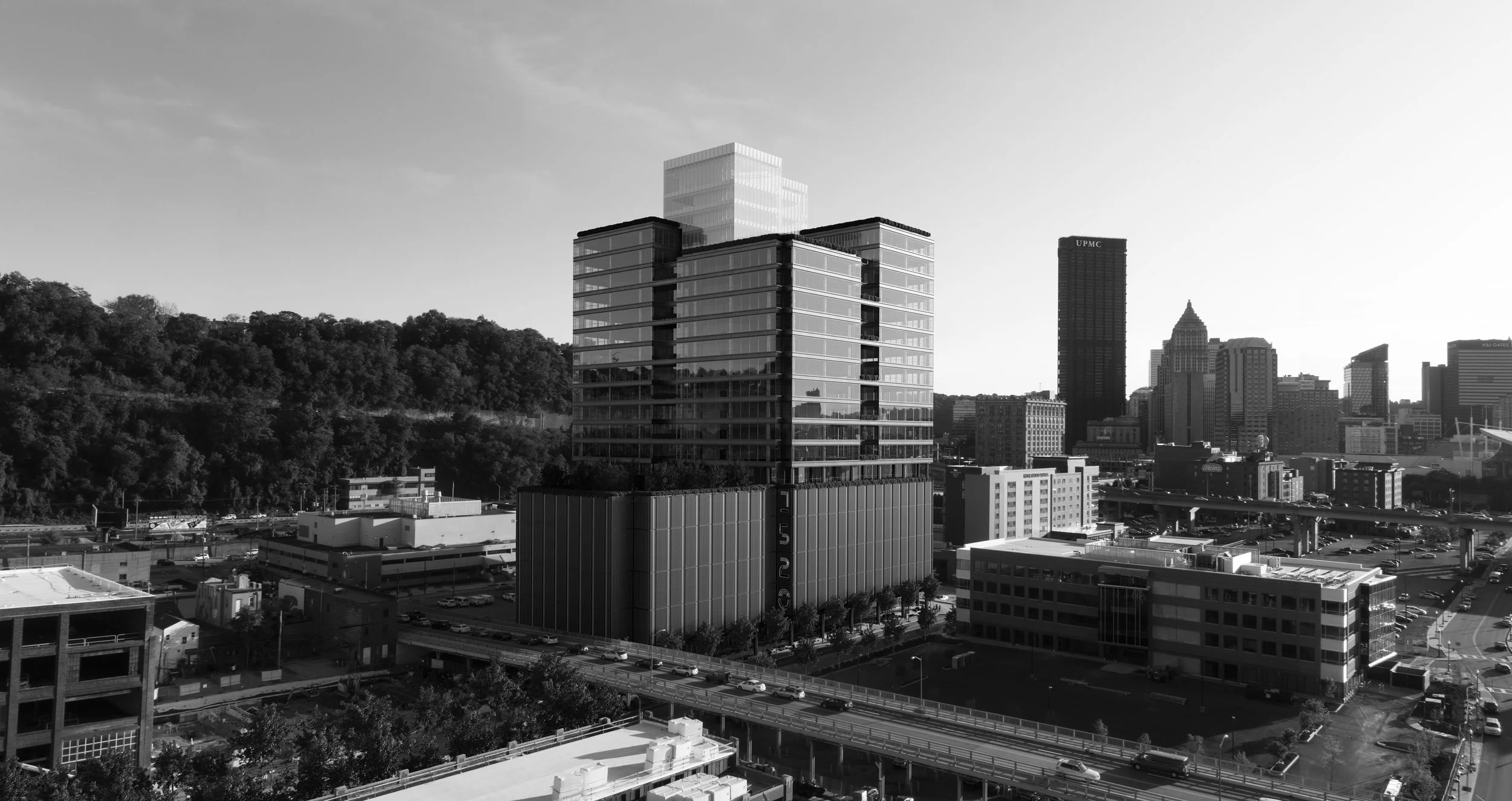 Black and white cityscape featuring modern high-rise buildings, a wooded hillside in the background, and a busy highway with cars.