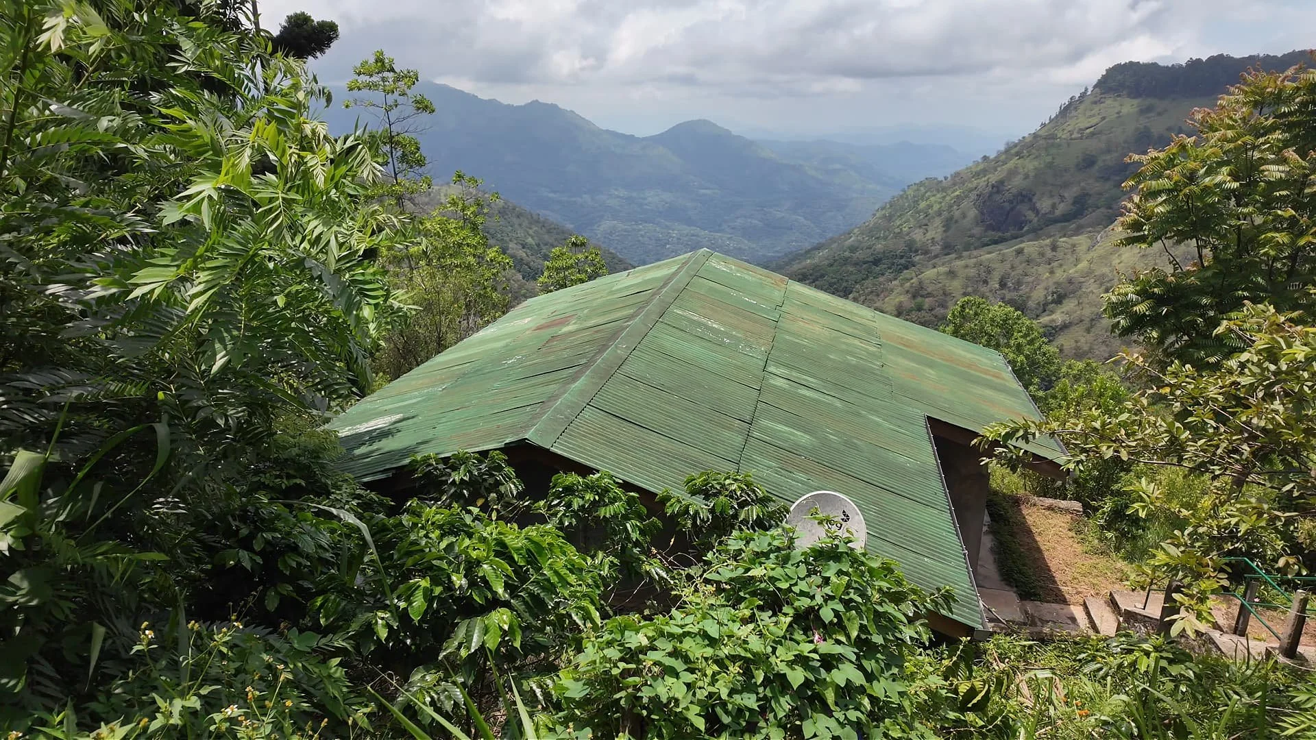 One of the cottages of Roseland Cottages in hill country in Sri Lanka. The cottage with green roof has an amazing view in the lush hills and is surrounded by coffee plants.