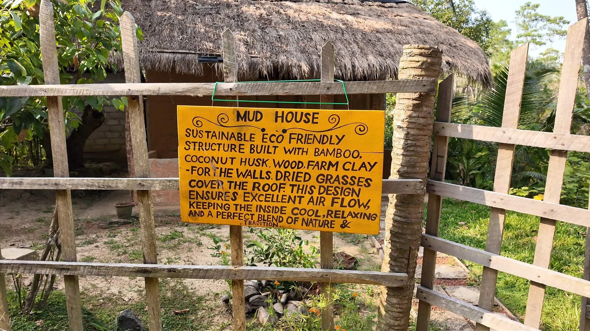 A fence and behind it a mudhouse made from mus, dried grass, bamboo and coconut husk at midigama fruit farm