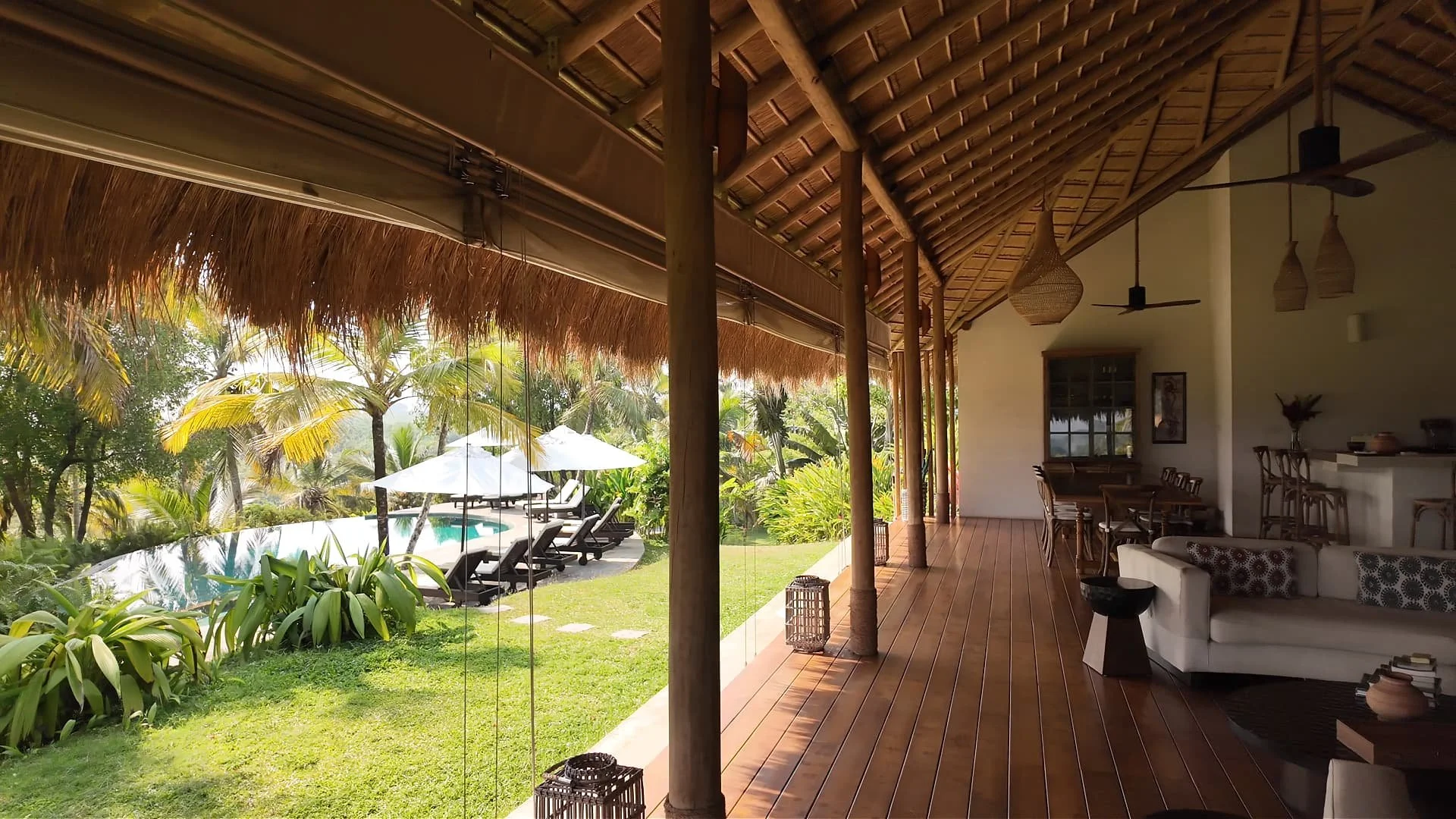 Open recepetion with woorden furniture and iluk grass on the roof and a pool alongside coconut trees