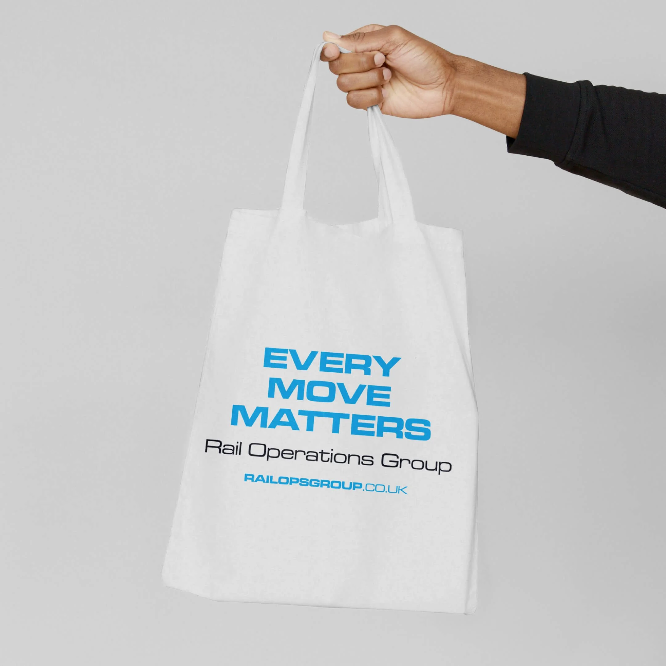 Person holding a white tote bag with blue and black text that reads "Every Move Matters" and "Rail Operations Group," with a gray background.