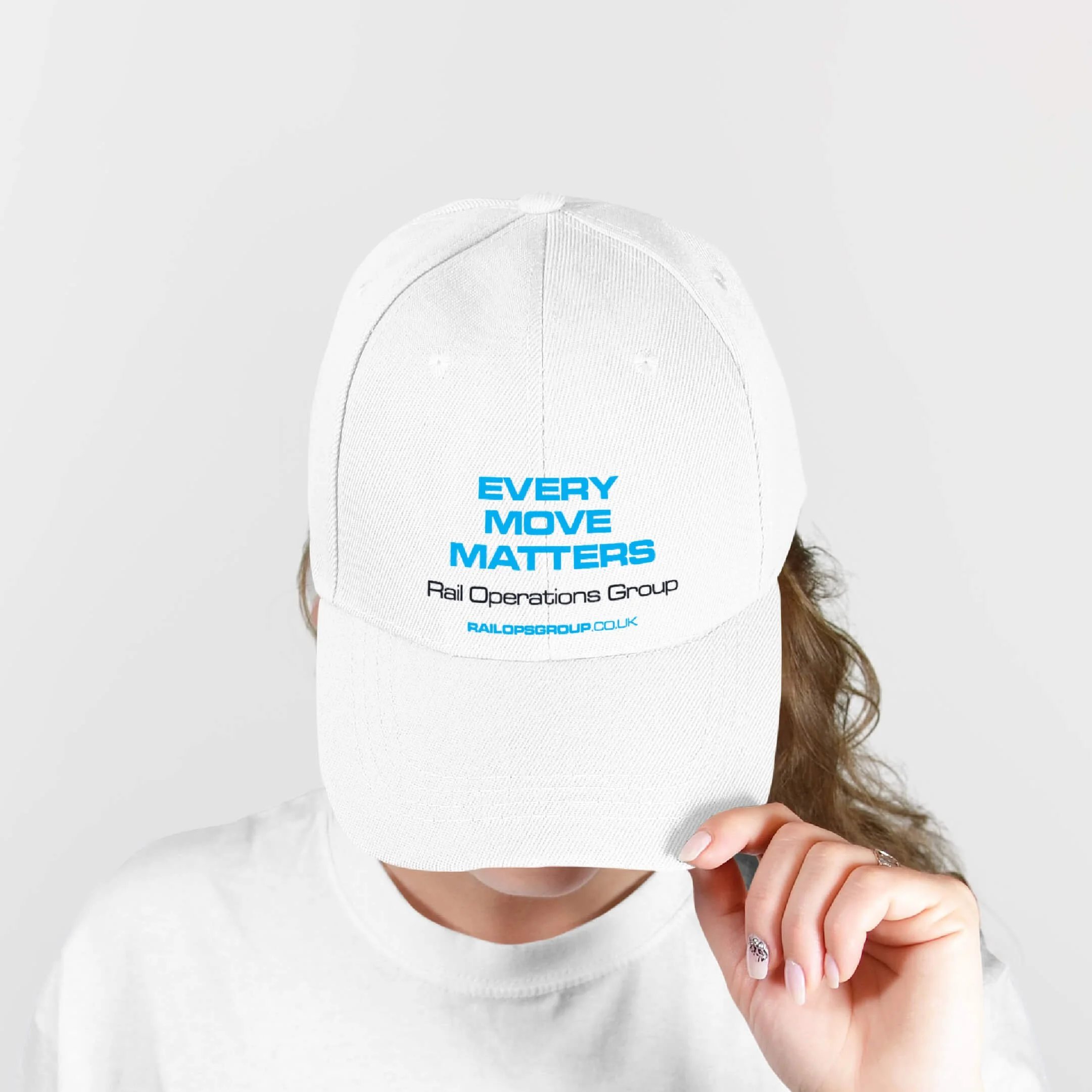 Person holding a white baseball cap with blue and black text, covering their face. The cap reads "Every Move Matters" and "Rail Operations Group" with a website URL.