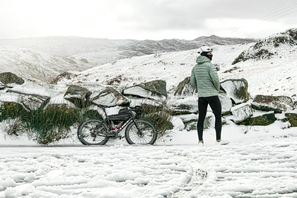 Daniil looking out over the snowy valley, his bike resting against the rocks