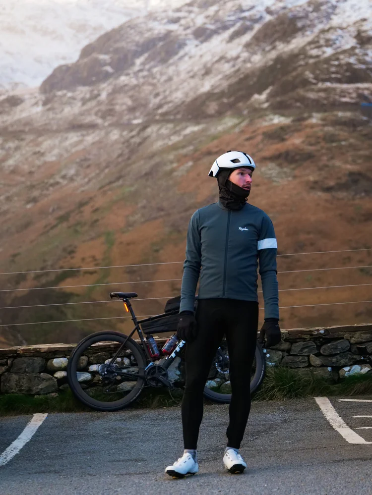 Daniil standing by his bike in a car park, a snowy mountain behind