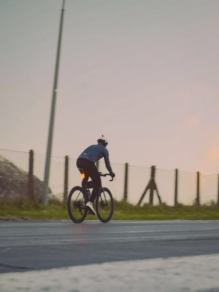 Daniil riding away down an empty road at sunrise