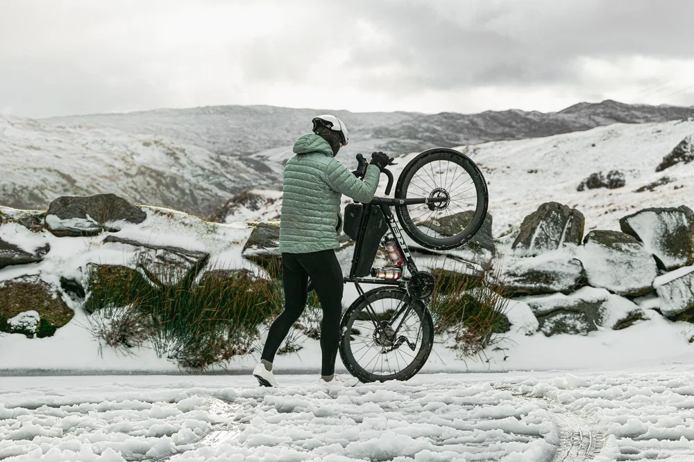 Daniil lifting his bike over a snowy roadside wall