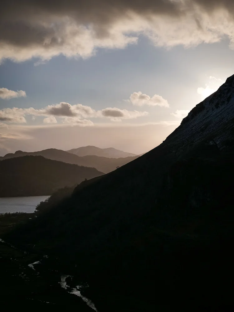 Sun breaking through cloud over a dark Welsh valley and lake