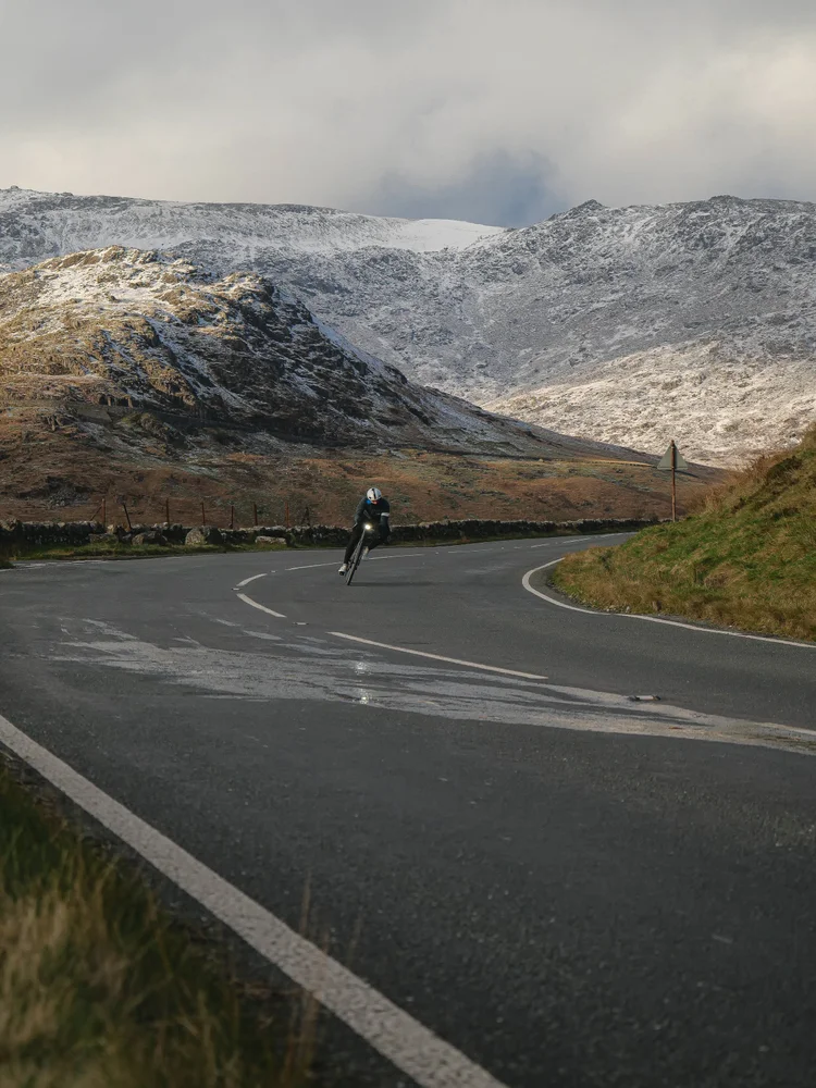A lone rider on a sweeping mountain road beneath snowy peaks