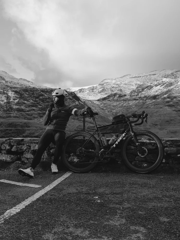 Black and white of Daniil leaning on a wall beside his bike in a mountain lay-by