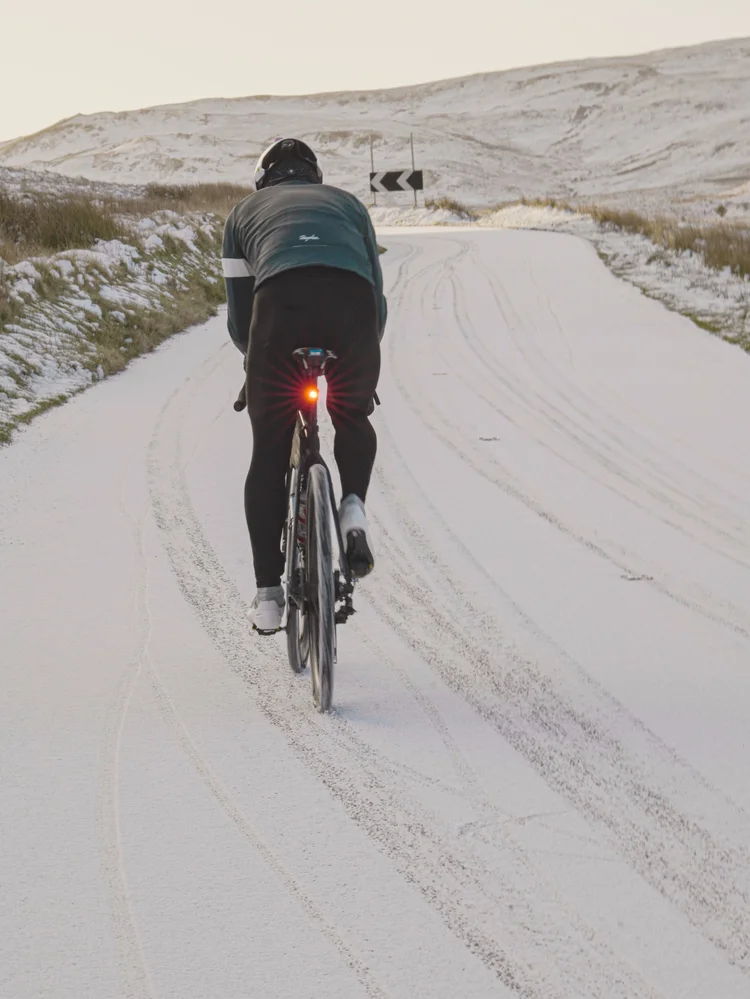 Daniil riding up a snow-covered road, rear light glowing