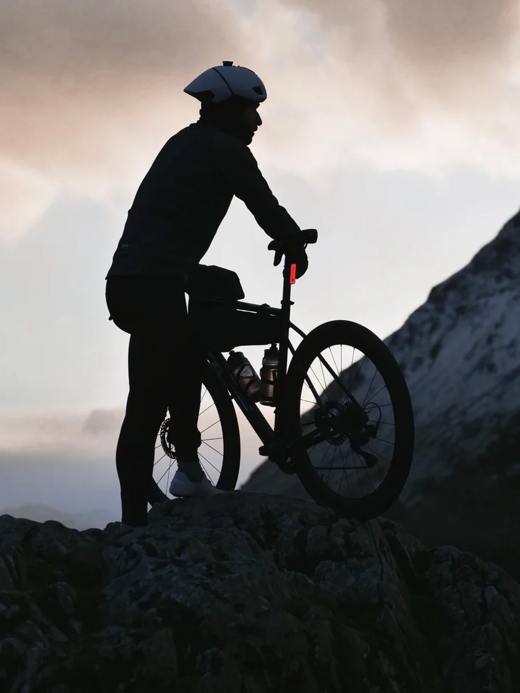 Daniil silhouetted with his bike on a rocky outcrop at dusk