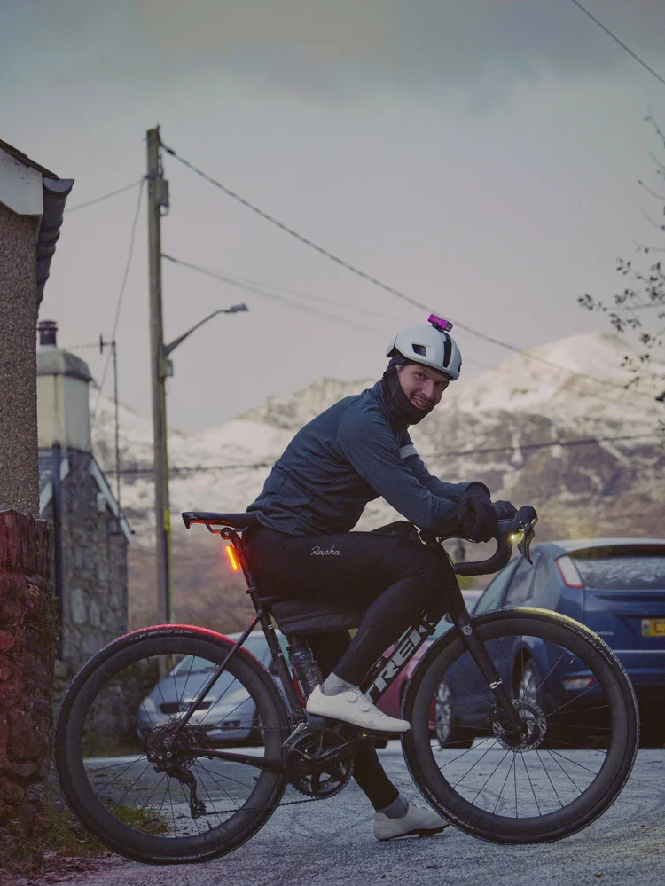 Daniil on his bike on a village street at dawn, mountains behind