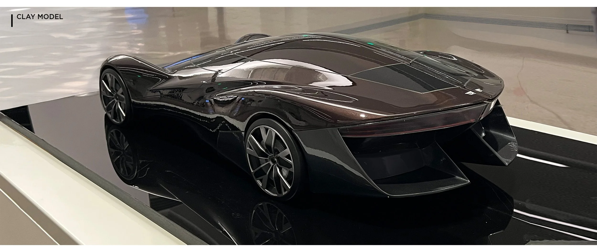 A sleek, black clay model of a futuristic sports car displayed on a black reflective surface at an exhibition.