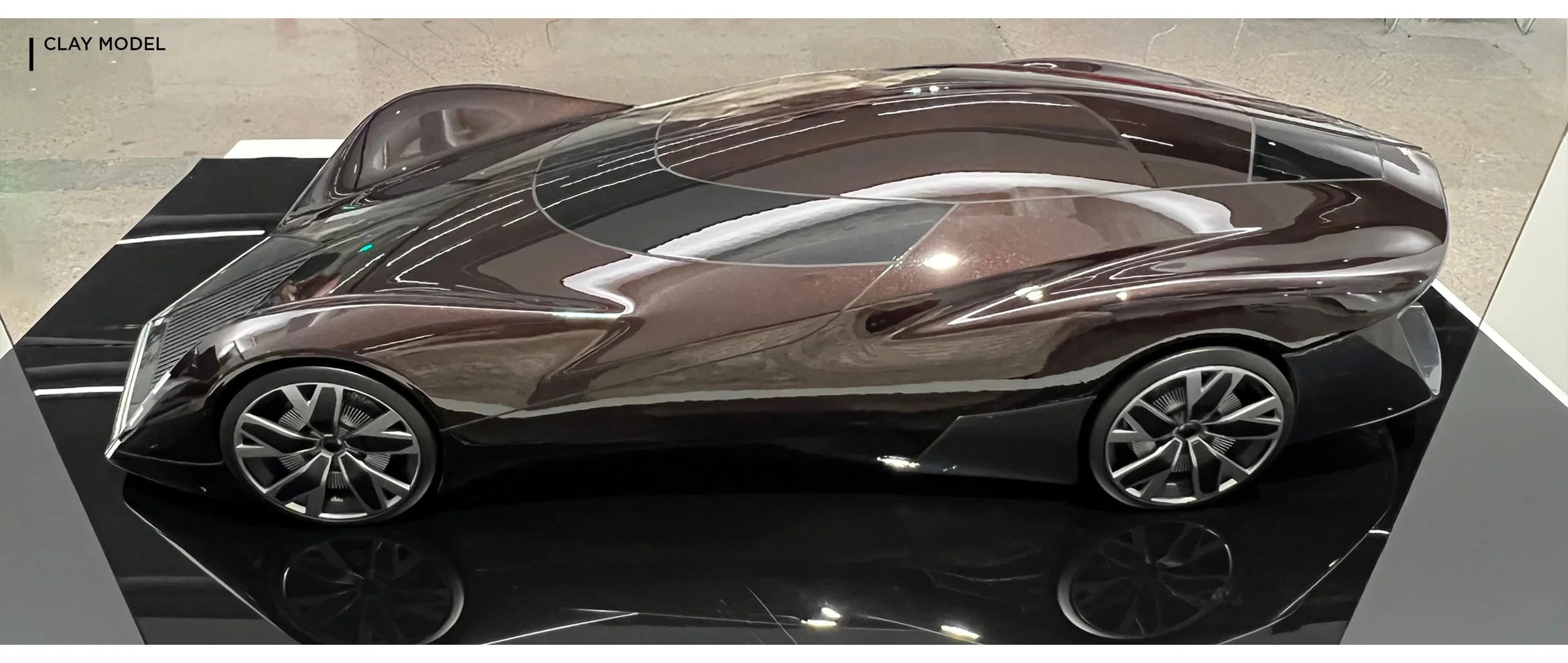 A sleek, futuristic concept car with a dark, reflective body and aerodynamic design on display at an exhibition.