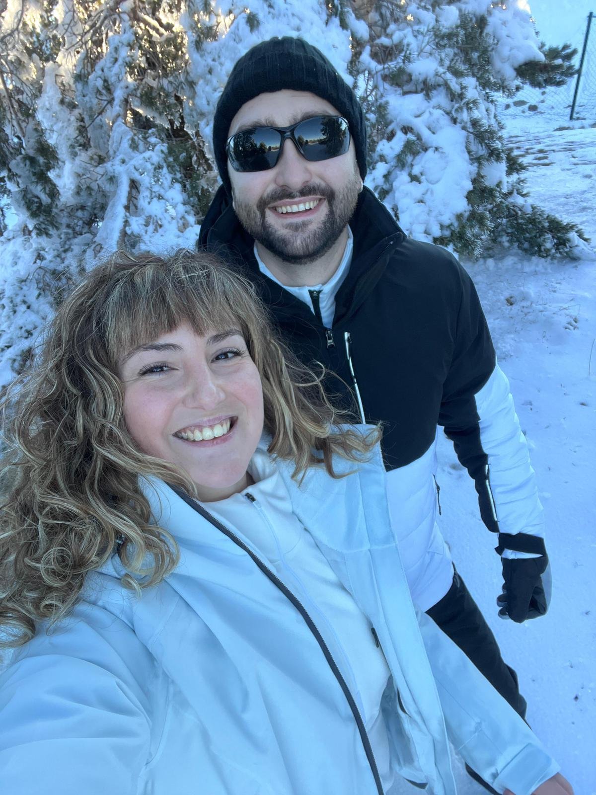 Los fotógrafos sonriendo en la nieve con árboles nevados y una cerca al fondo