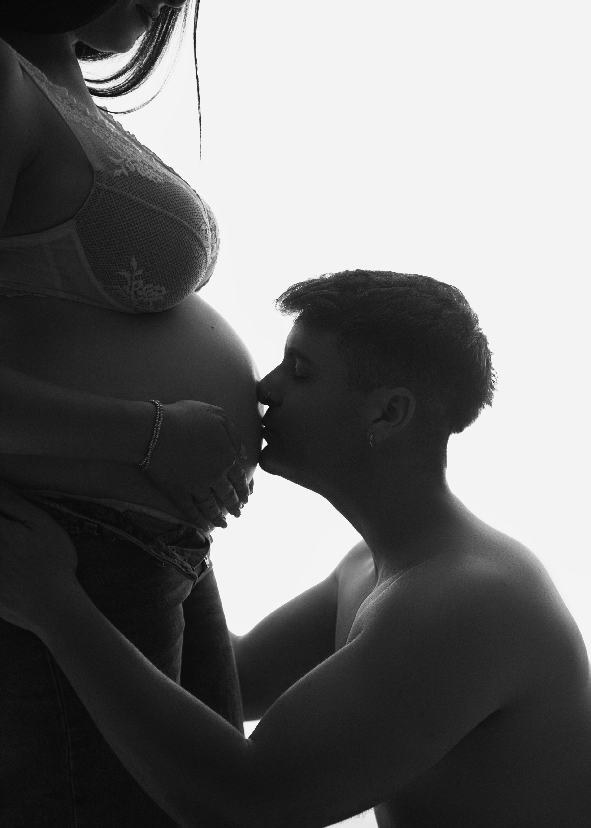 Una pareja en silueta, con la mujer embarazada y el hombre besando su vientre.